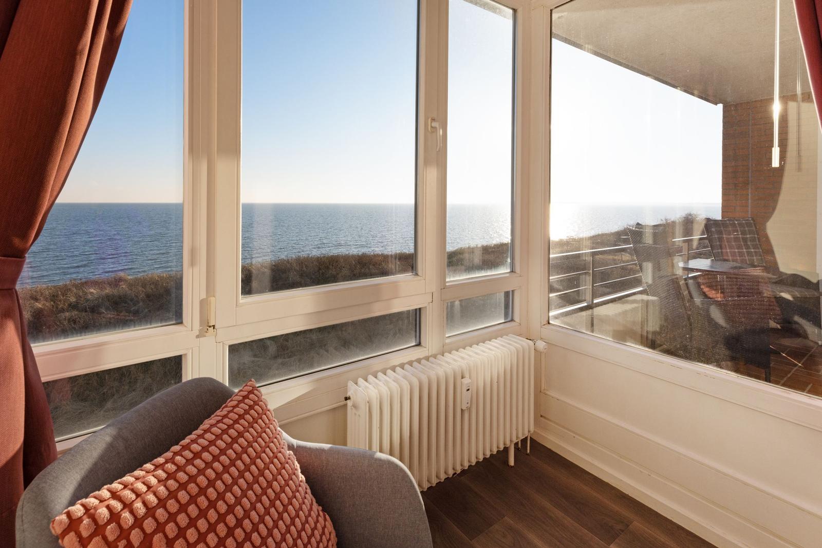Ein Raum mit Blick aufs Meer, große Fenster, Sitzgelegenheit und Balkon mit Tisch und Stühlen.