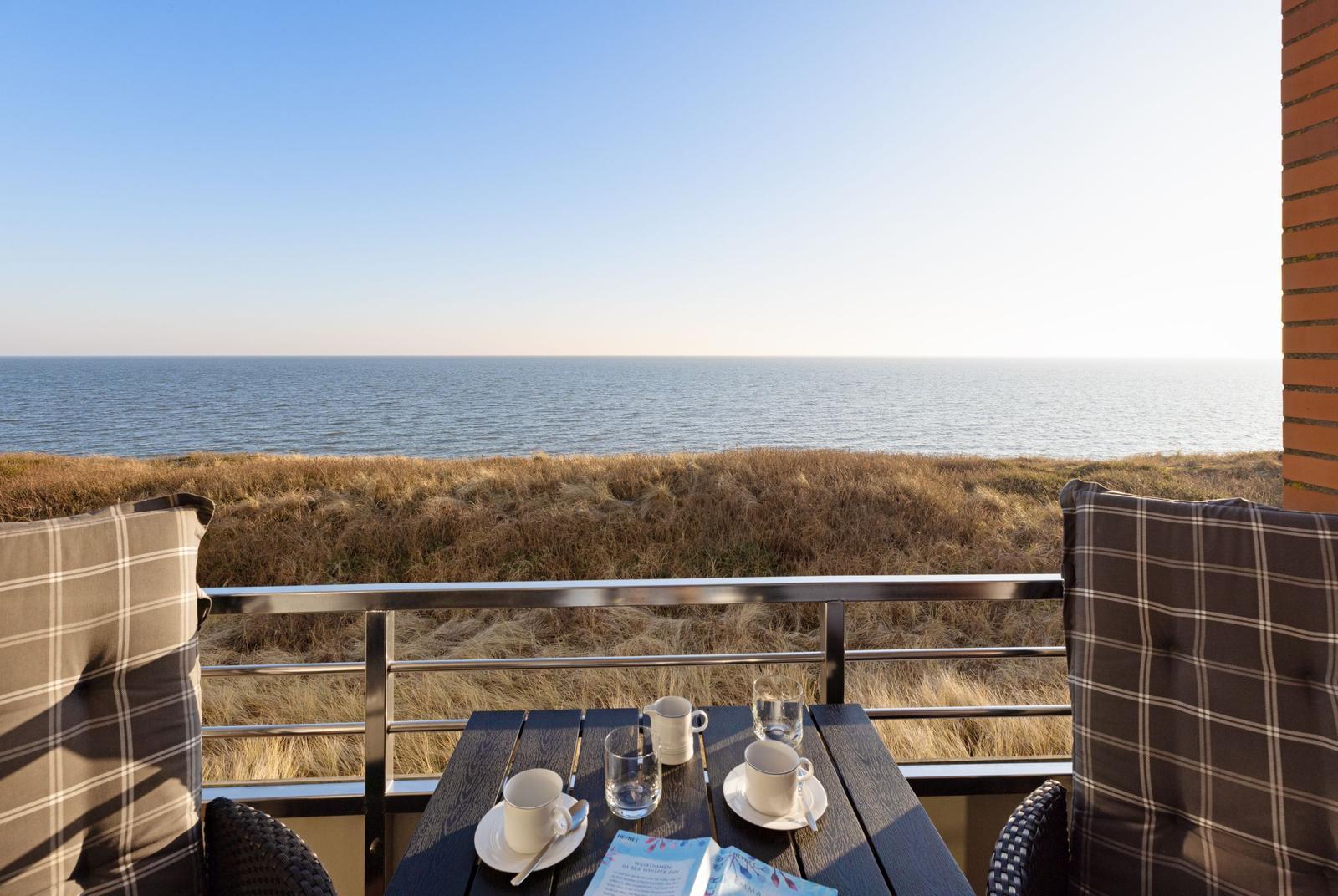 Terrasse mit Tisch und Stühlen, Blick auf das Meer und trockenes Gras.