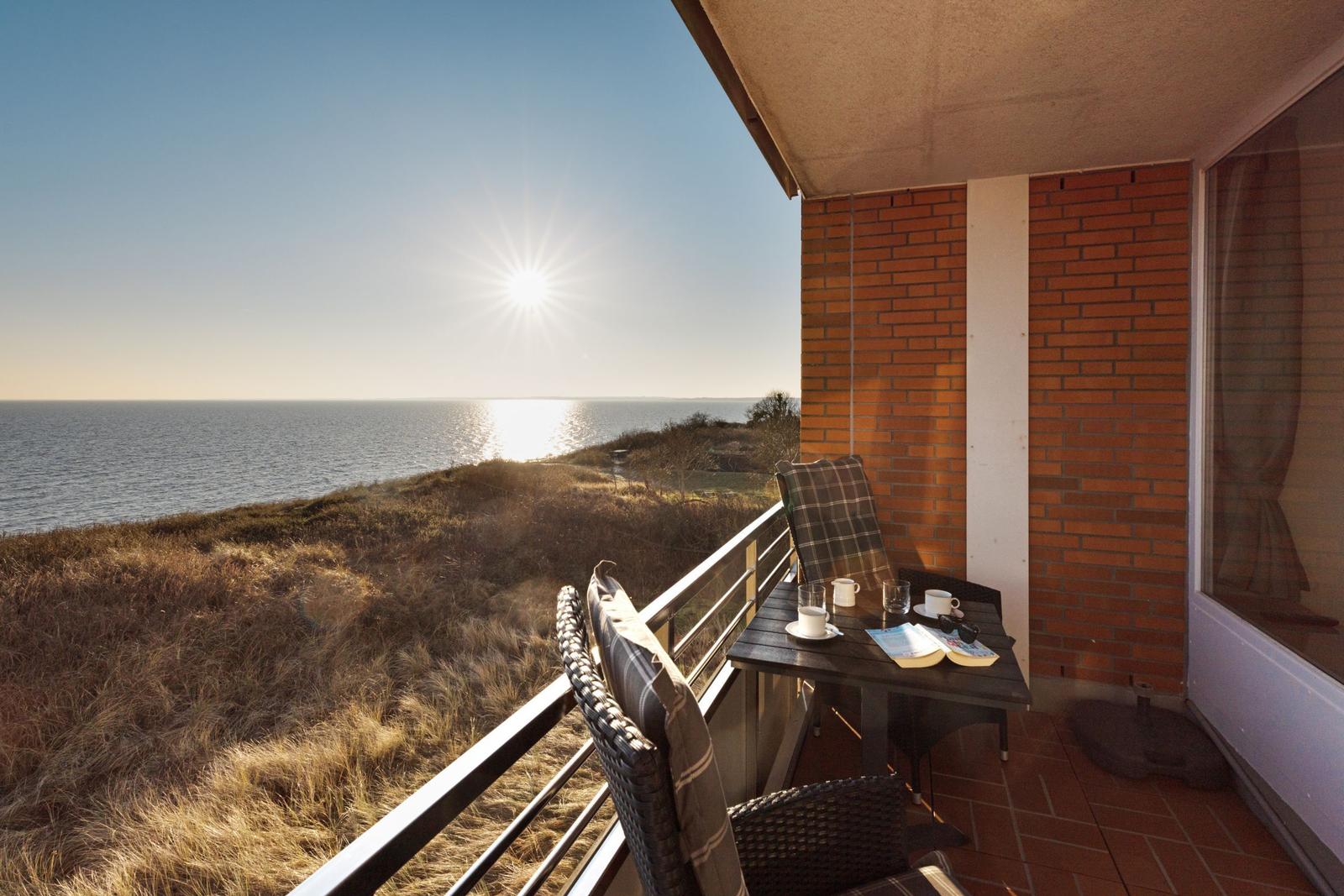 Terrasse mit Meerblick, Tisch und Stühle, Sonne scheint über dem Meer.