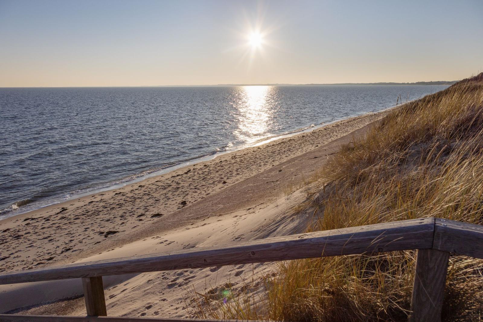 Sonniger Strand mit Dünen und Holzgeländer. Blick auf das Meer bei Sonnenuntergang.
