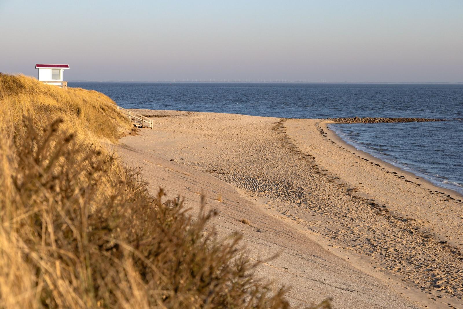 Strand mit Dünen, kleinem Haus und Blick aufs Meer.