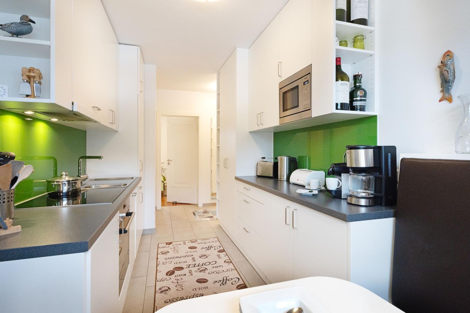 Küche mit weißen Schränken, grüner Rückwand und Küchenzeile
