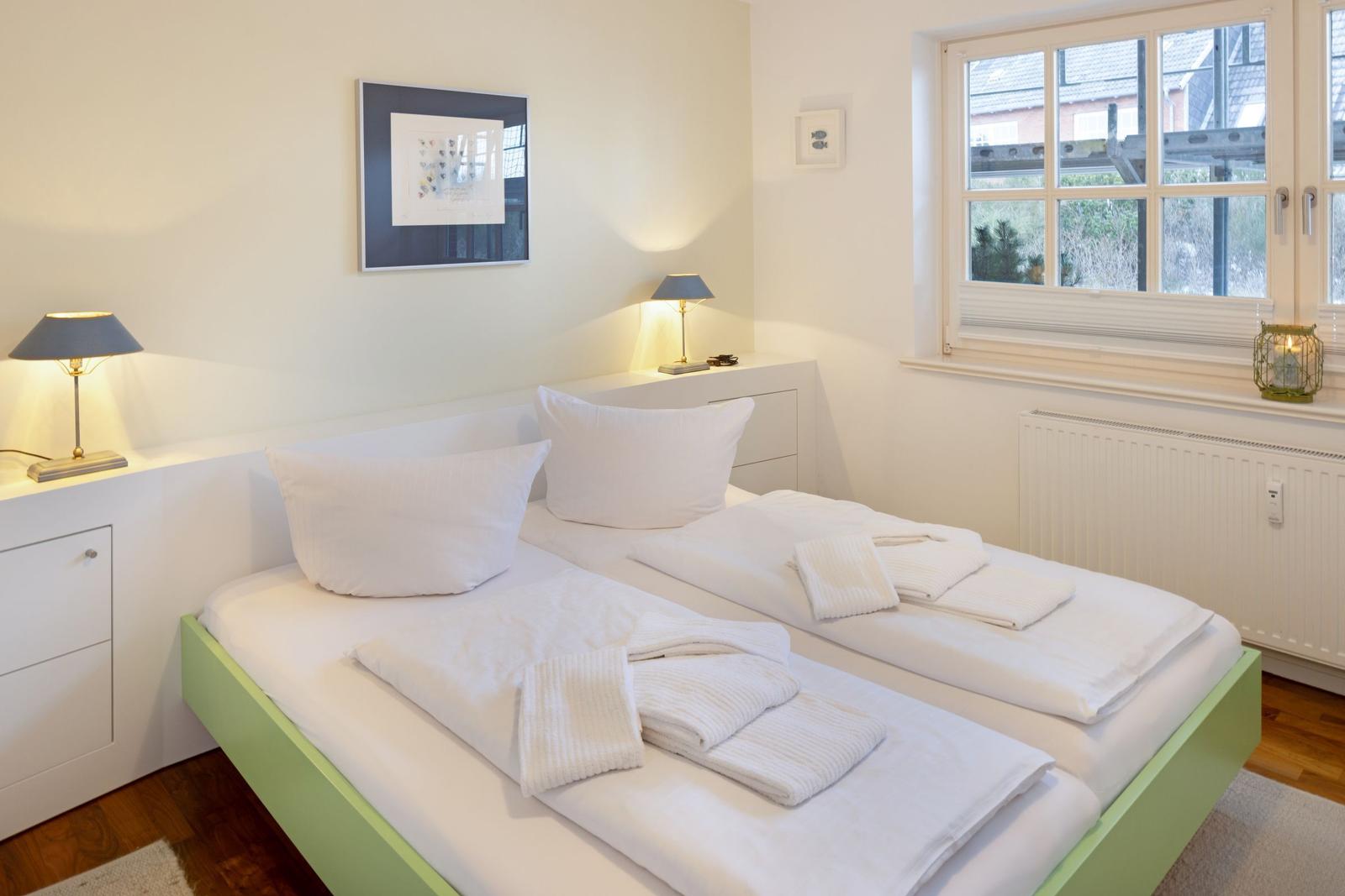 Zwei Betten mit weißen Laken und Handtüchern. Fenster mit Blick nach draußen.