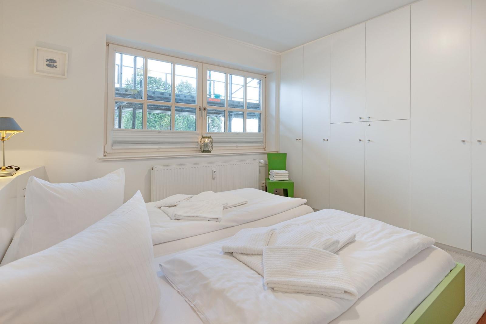 Schlafzimmer mit Doppelbett, weißen Wänden und großen Fenstern.