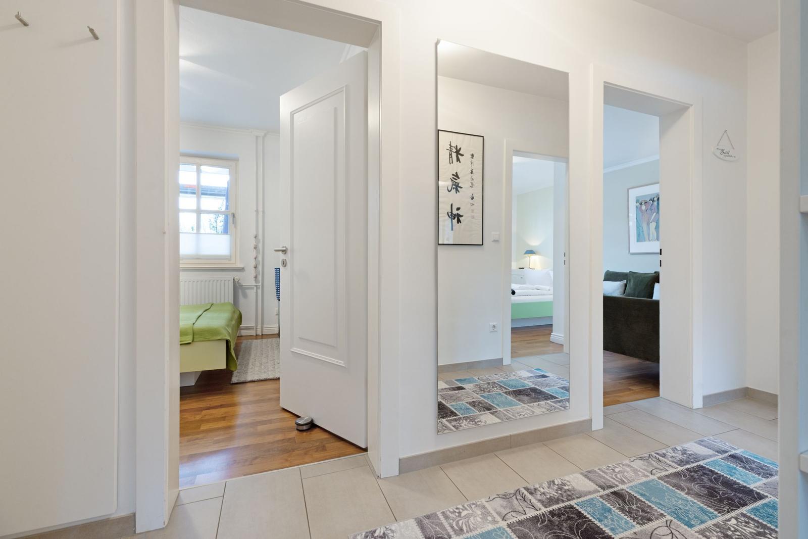 Flur mit Blick in Schlafzimmer und Wohnbereich. Teppich und Wandbilder sichtbar.
