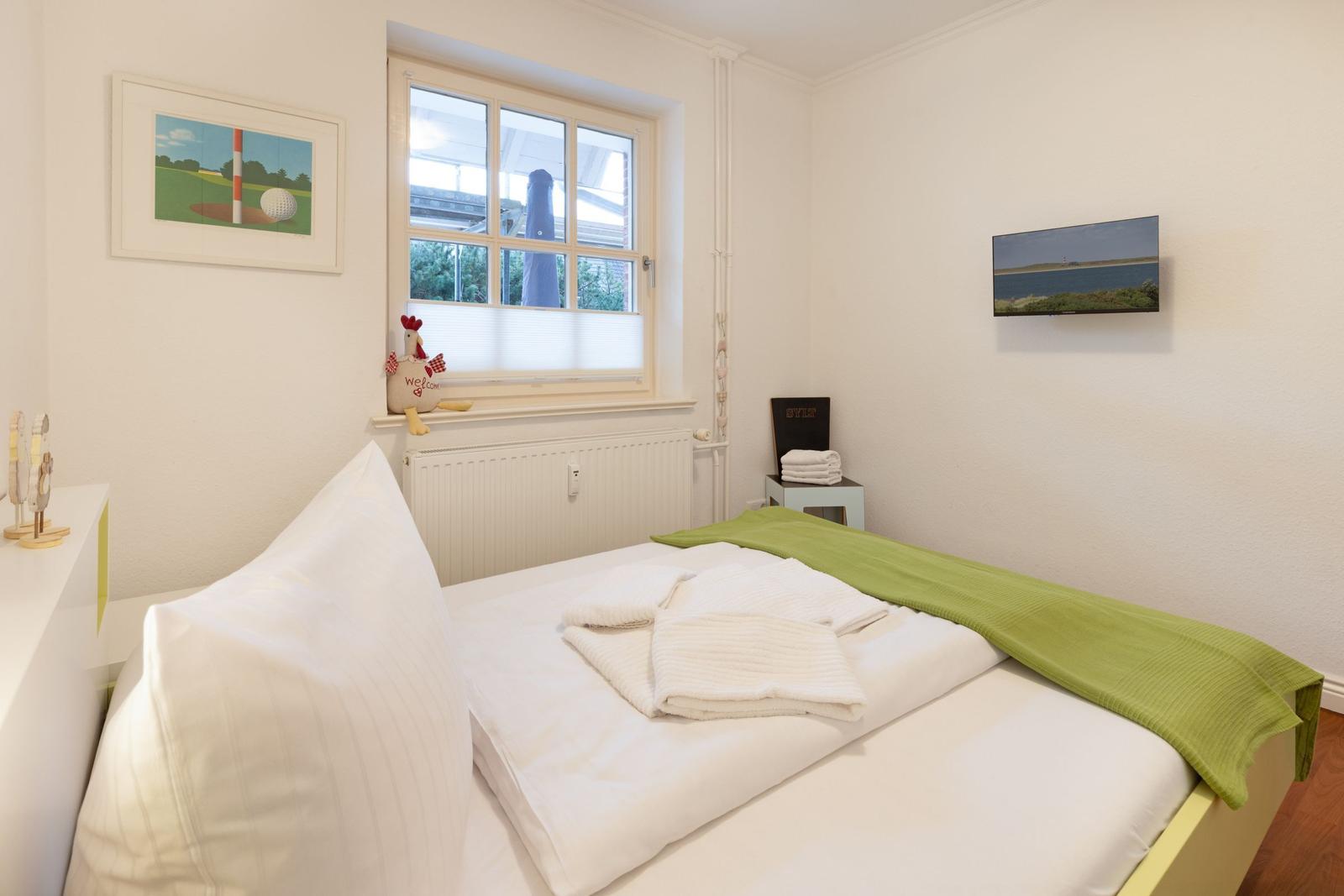 Schlafzimmer mit Bett, Fenster und Wandbildern.