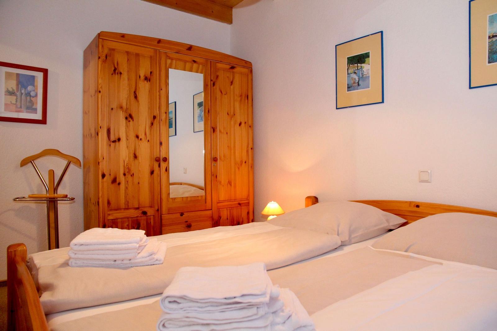 Schlafzimmer mit Holzbett, Kleiderständer und Kleiderschrank mit Spiegeltür.