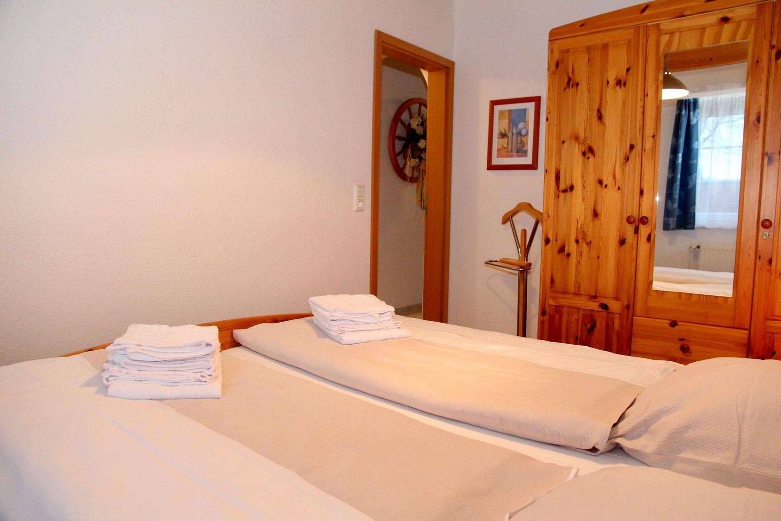 Schlafzimmer mit Bett, Holzschrank und Handtüchern.