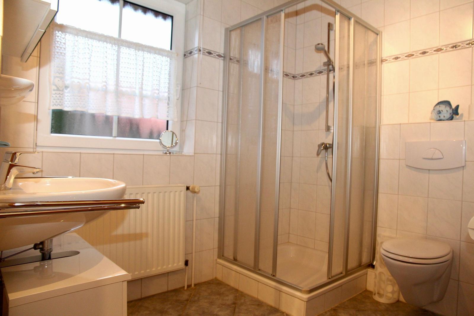 Badezimmer mit Dusche, Waschbecken und Toilette. Fenster mit Vorhang.