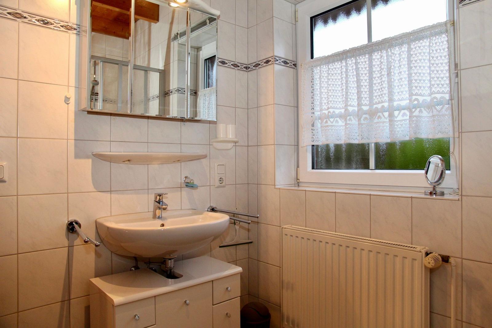 Badezimmer mit Waschbecken, Spiegel und Fenster mit Vorhang.