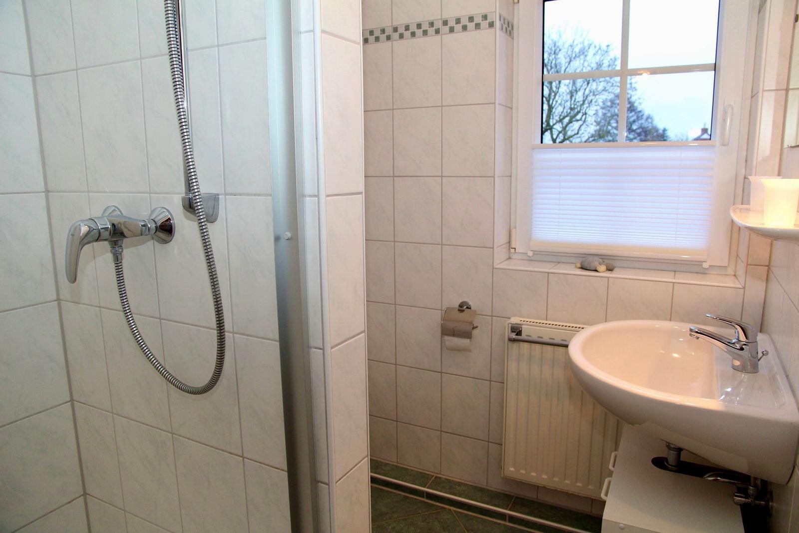 Badezimmer mit Dusche, Waschbecken und Fenster.
