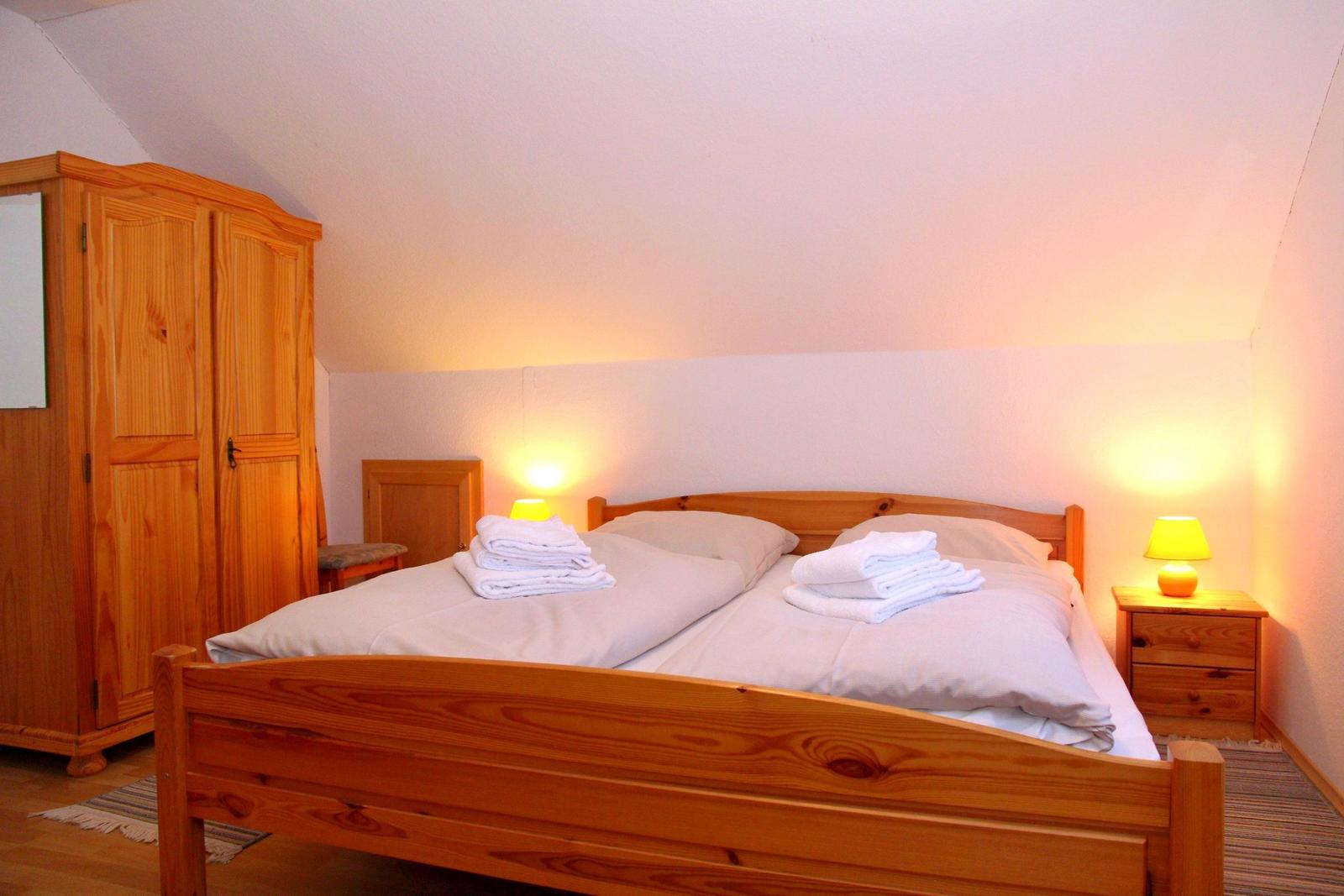 Ein Schlafzimmer mit Holzbett, Nachttischen und Kleiderschrank unter Dachschrägen.