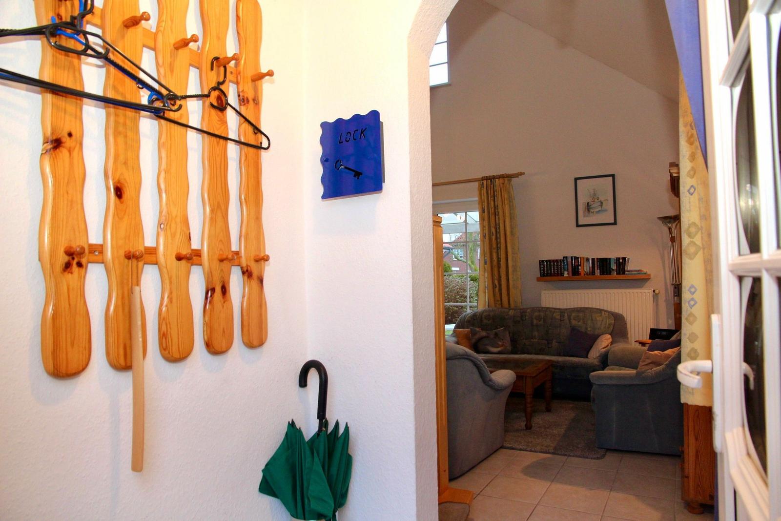 Eingangsbereich mit Holzgarderobe und Blick in das Wohnzimmer mit Sofa und Couch.