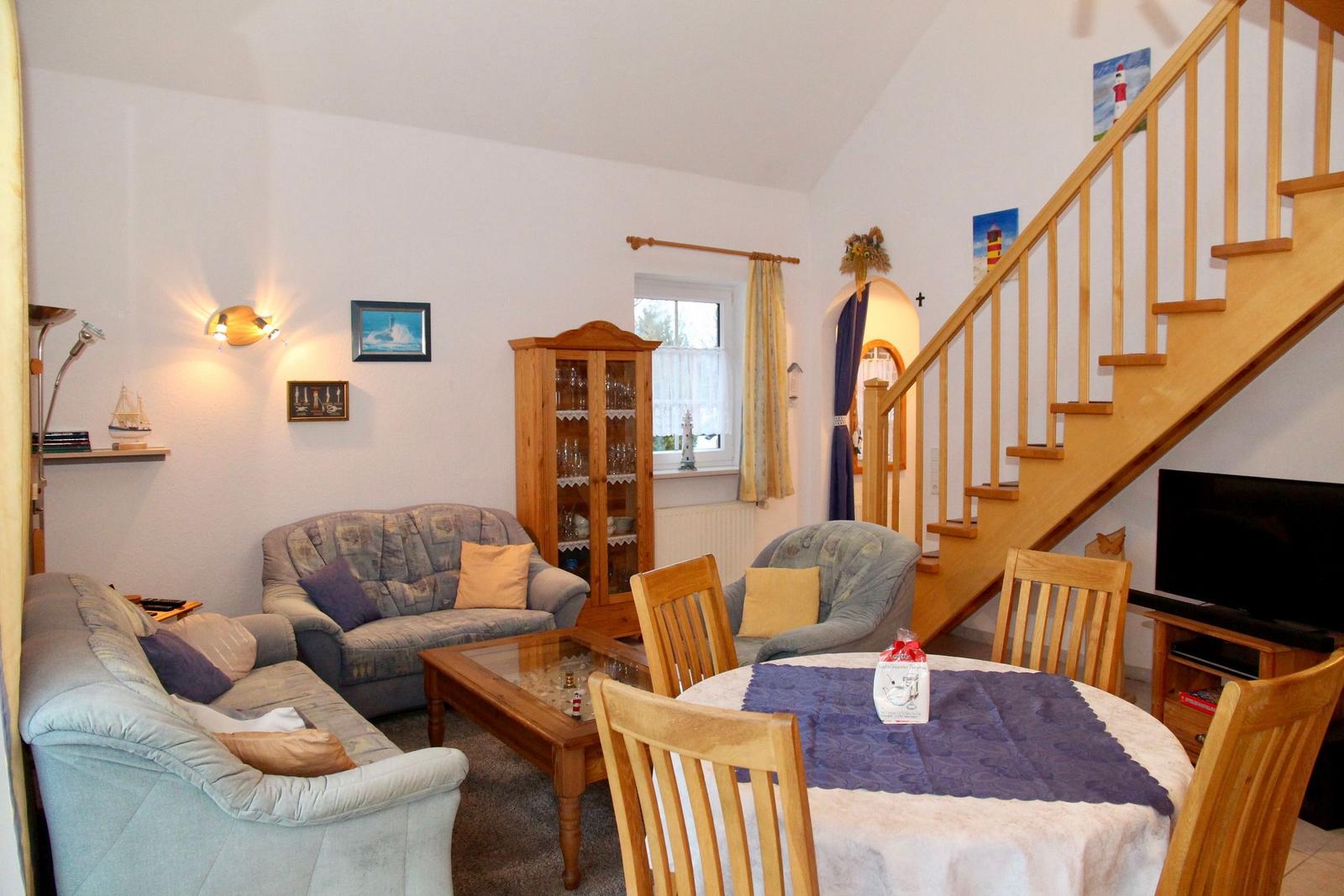 Wohn- und Essbereich mit Holztreppe, Sofa, Stühlen und Esstisch.