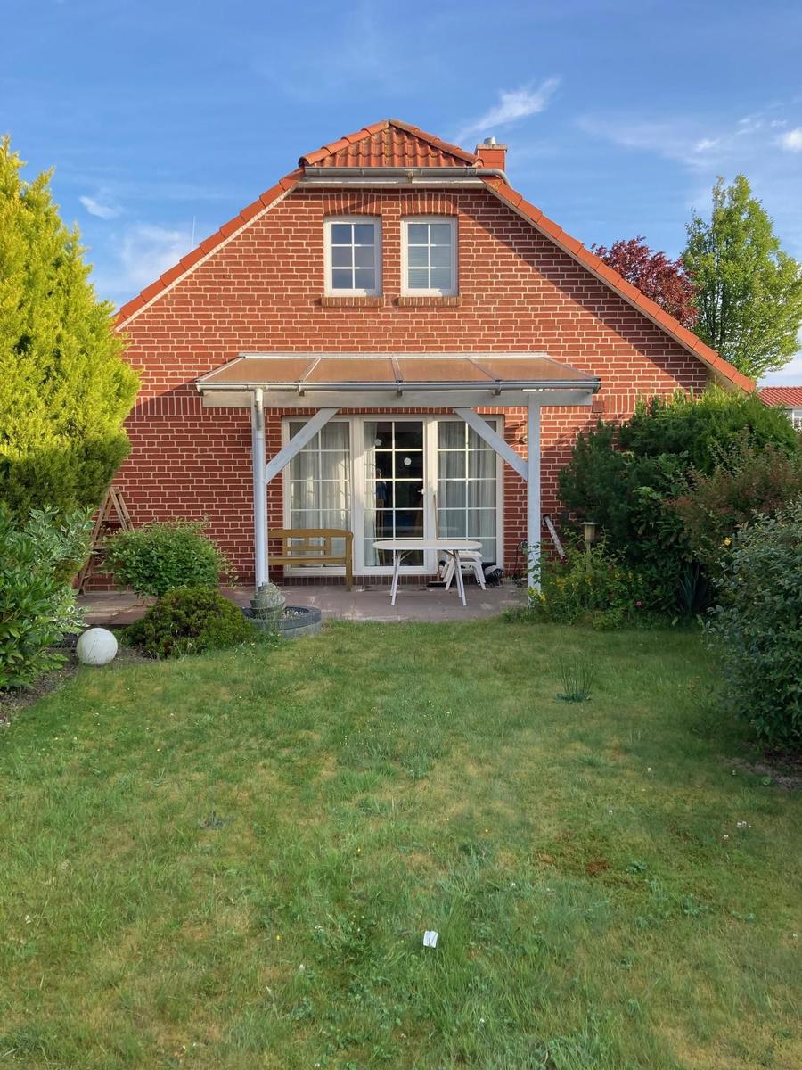 Rotes Backsteingebäude mit Terrasse und Garten. Weiße Fenster und Tür.