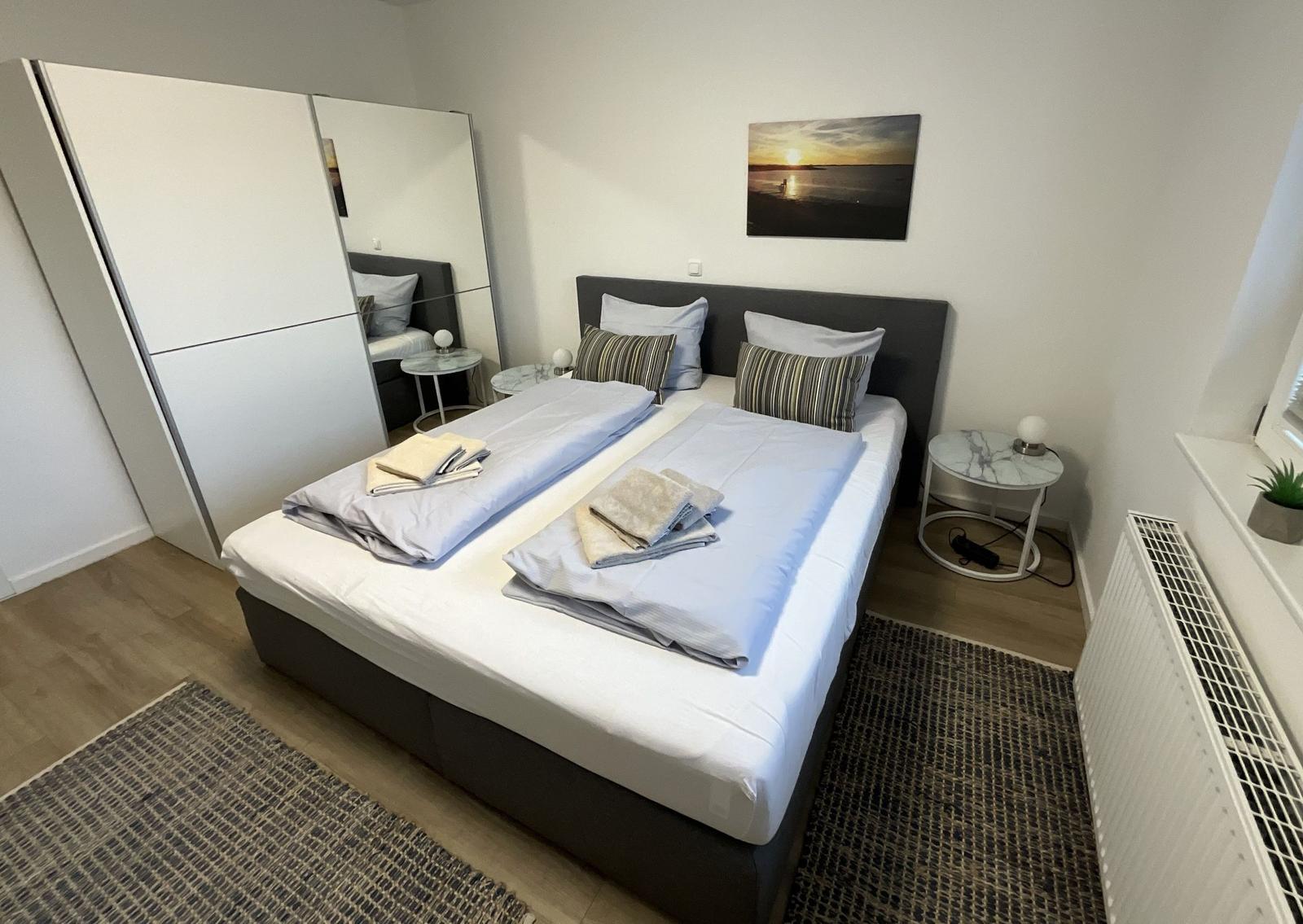 Schlafzimmer mit Doppelbett, Kleiderschrank und Wandbild.