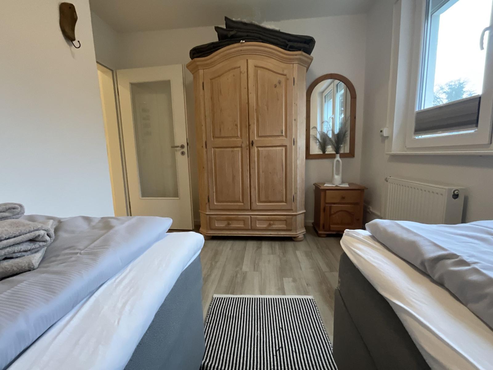 Zwei Betten, großer Holzschrank, Fenster und Bodenbelag