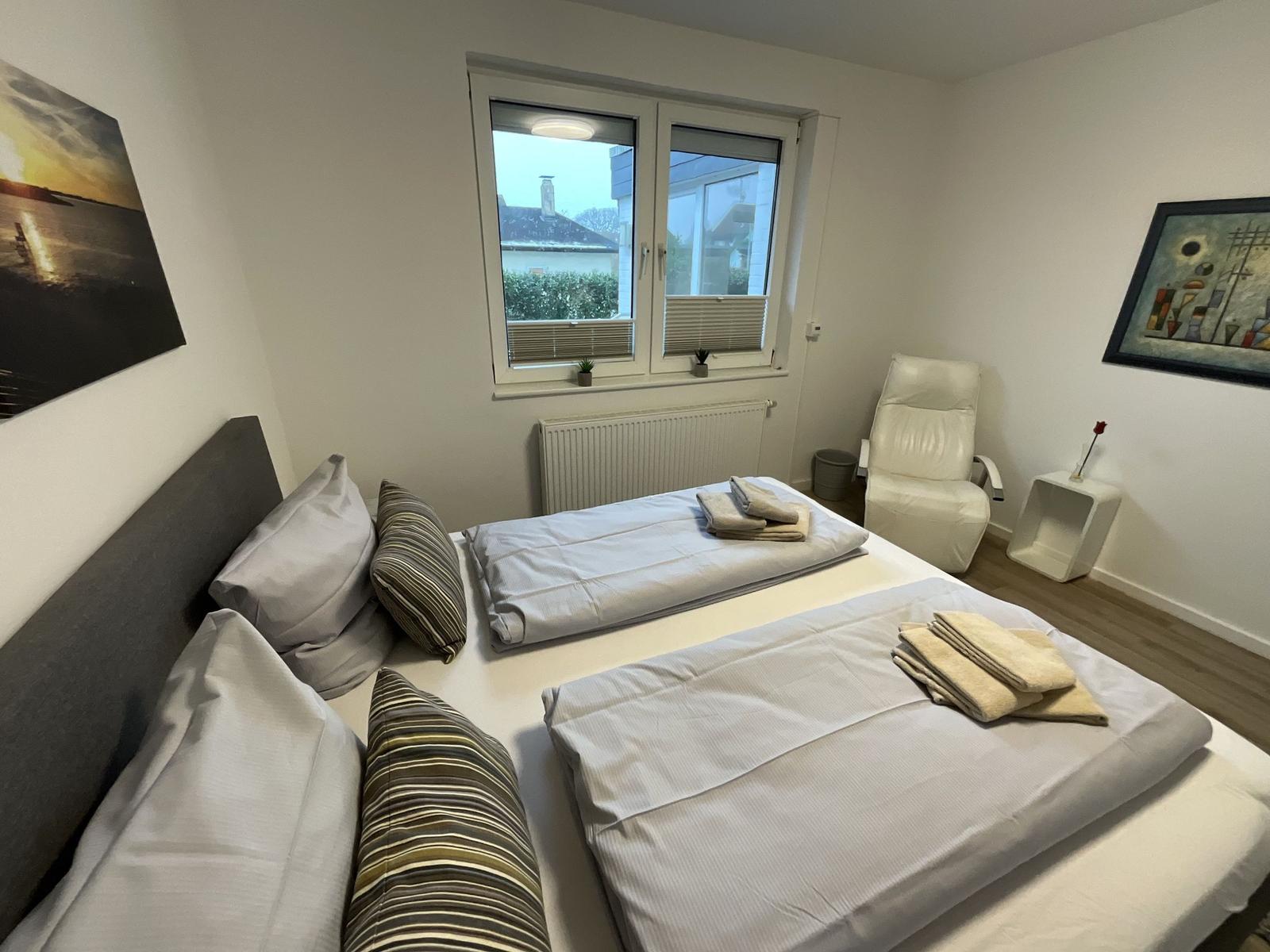 Zimmer mit Doppelbett, Fenster, Sessel und Wandbildern.