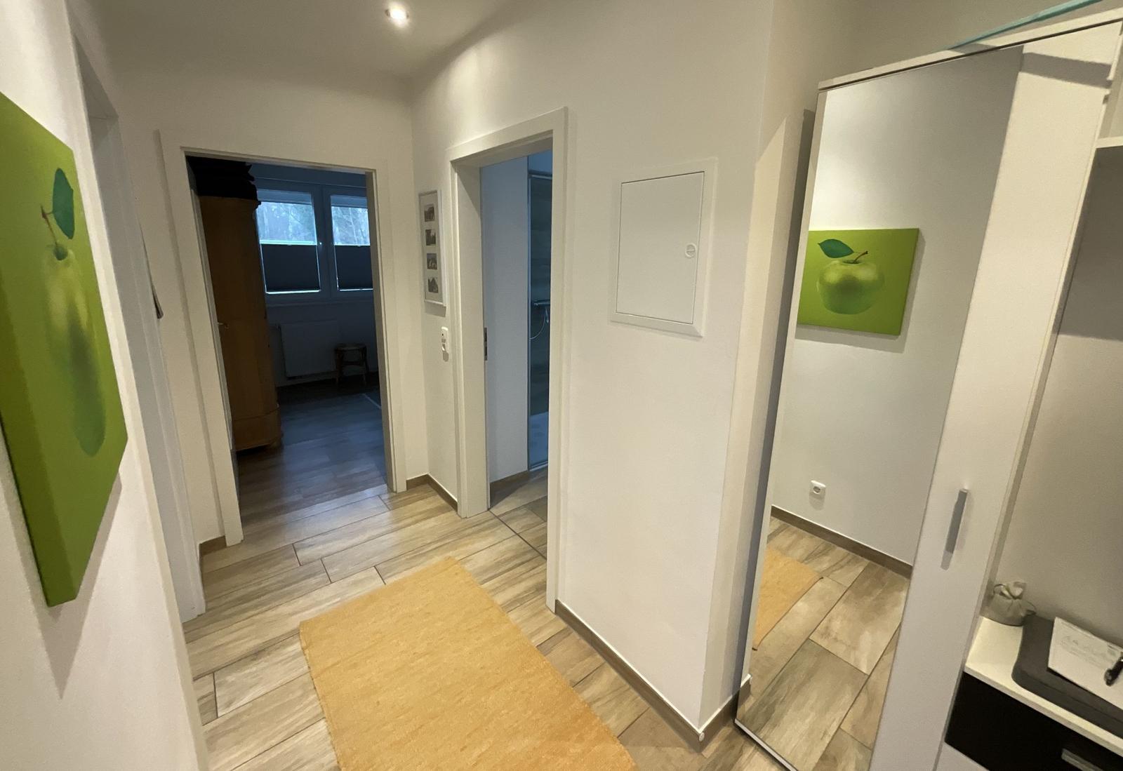 Flur mit Holzboden, Teppich und Spiegelschrank. Bilder an den Wänden.