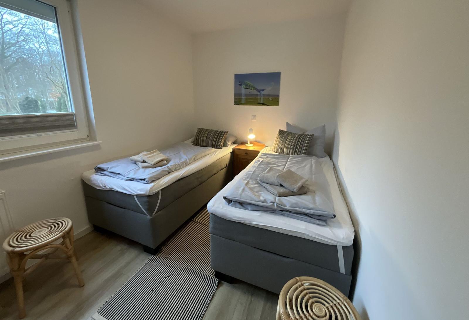 Zwei Einzelbetten mit Bettwäsche, Nachttisch und Fenster.