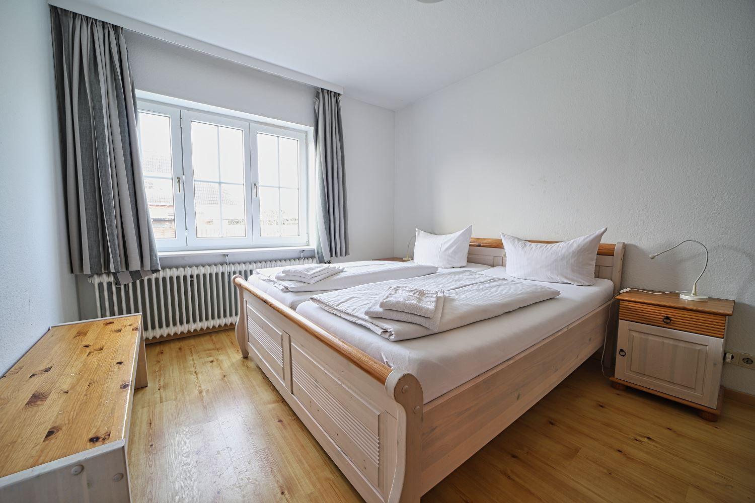 Schlafzimmer mit Holzbett, Fenster und Nachttisch.