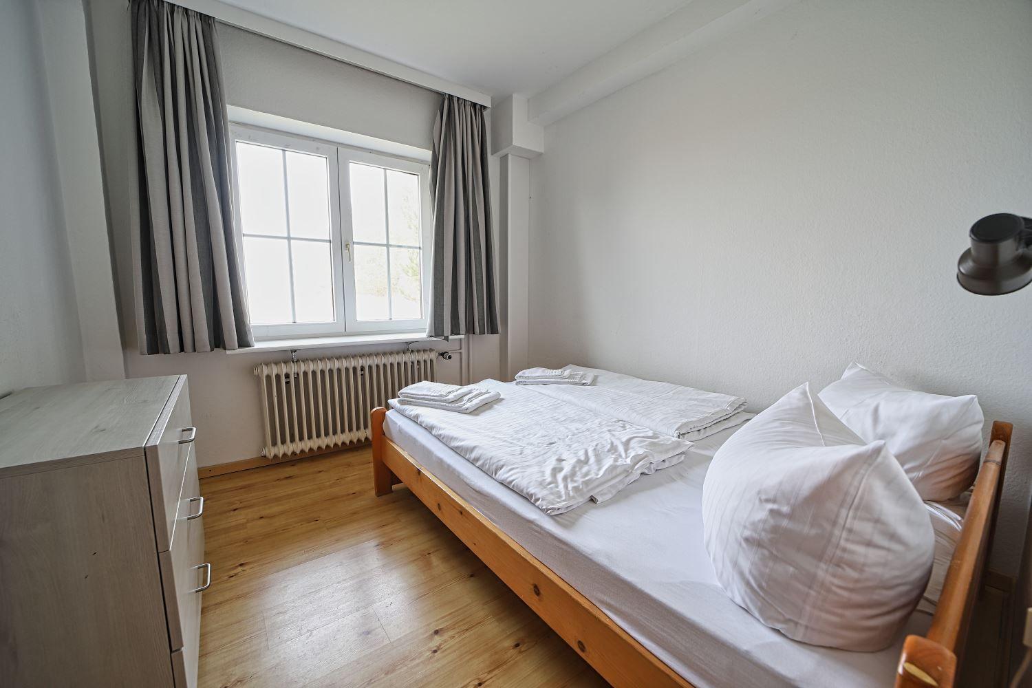 Schlafzimmer mit Bett, Kleiderschrank und Fenster mit Vorhängen.