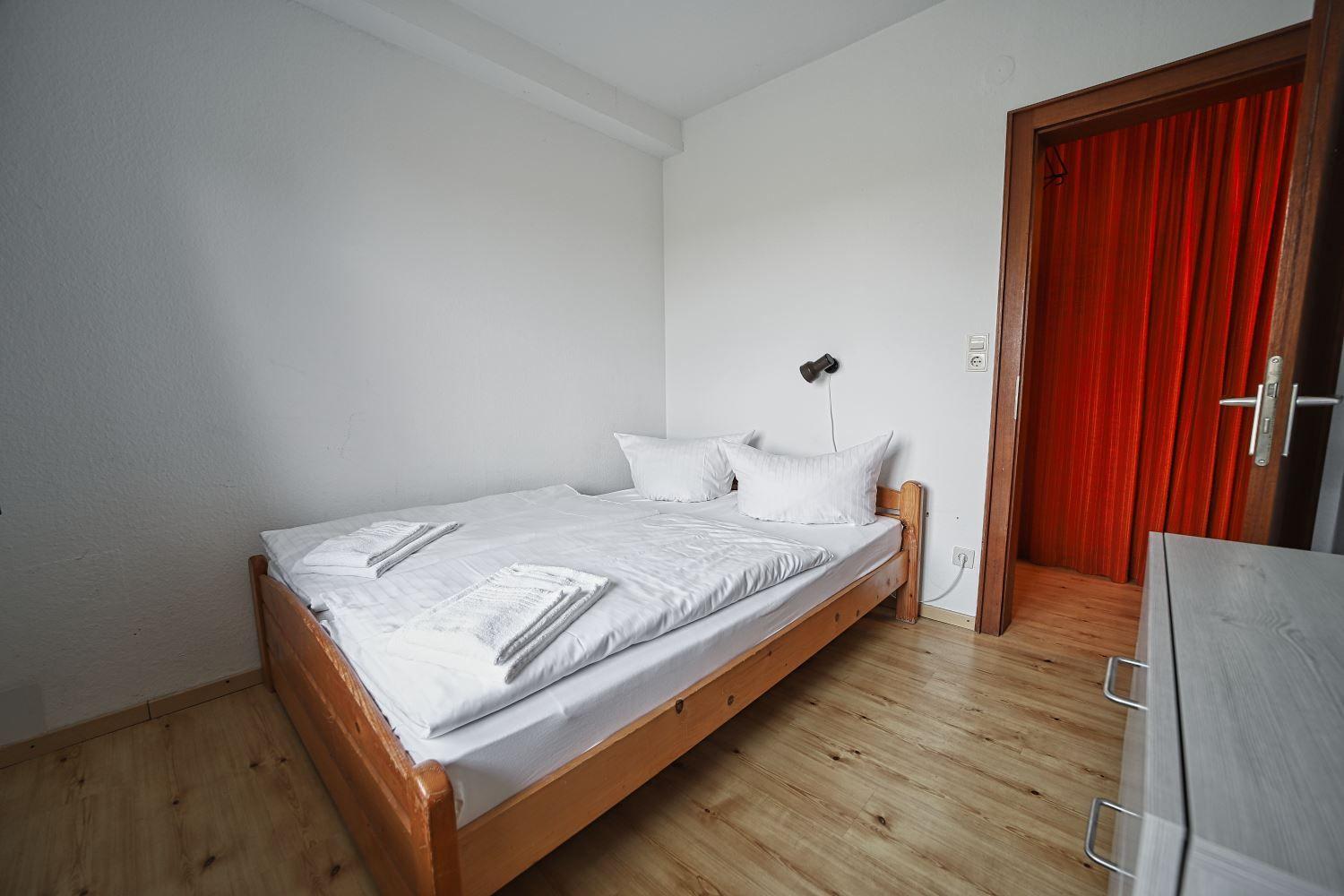 Schlafzimmer mit Bett, Holzboden und roter Türvorhang.