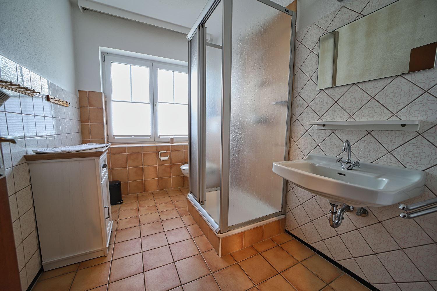 Badezimmer mit Dusche, Waschbecken und Fenster.