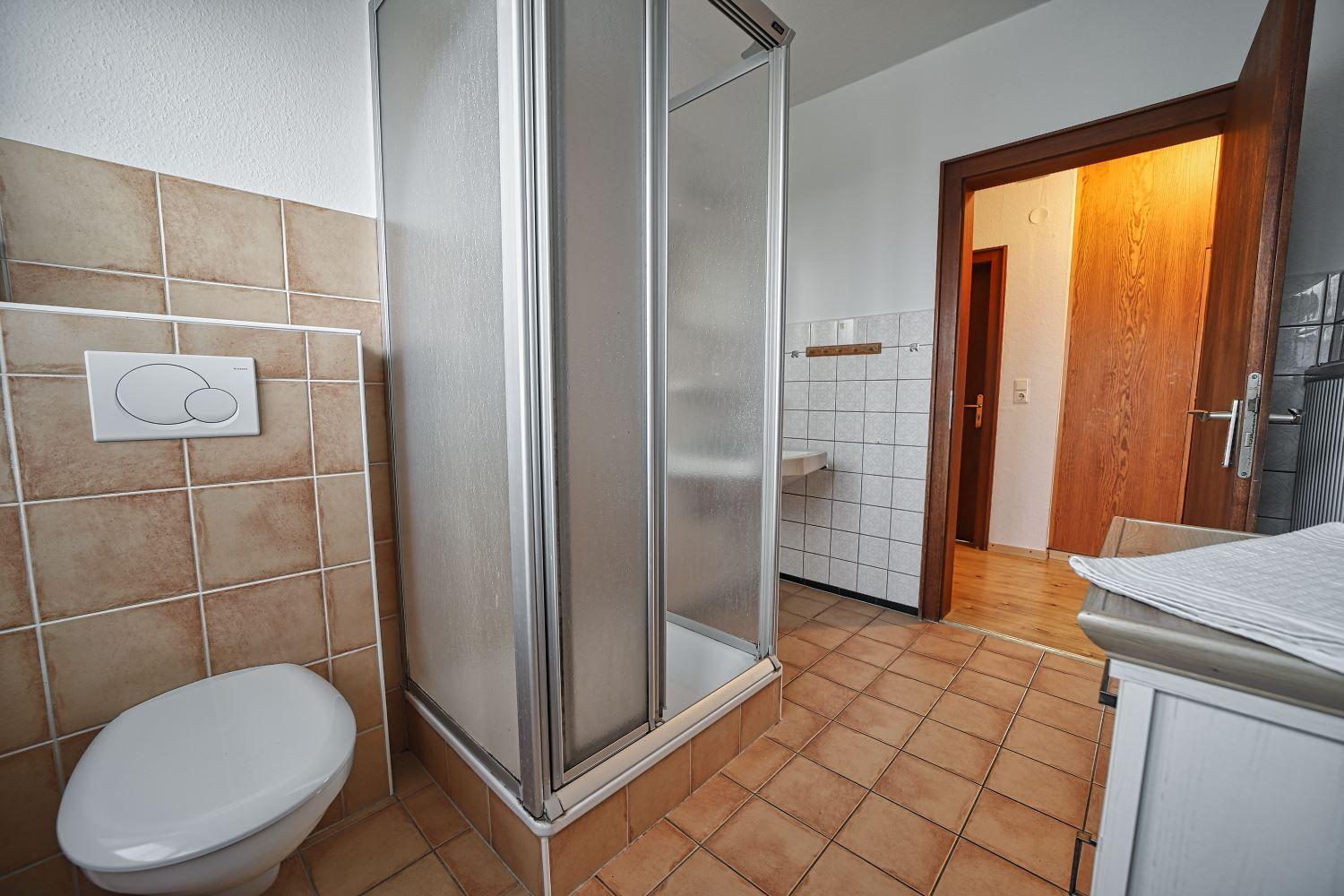 Badezimmer mit Dusche, Toilette und Waschbecken. Fliesenboden und -wände.