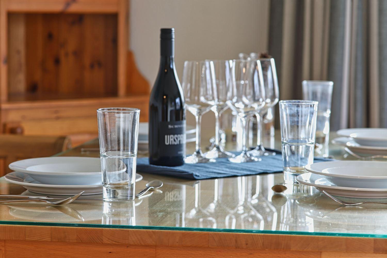 Glasplatte mit Teller, Gläsern und einer Weinflasche.