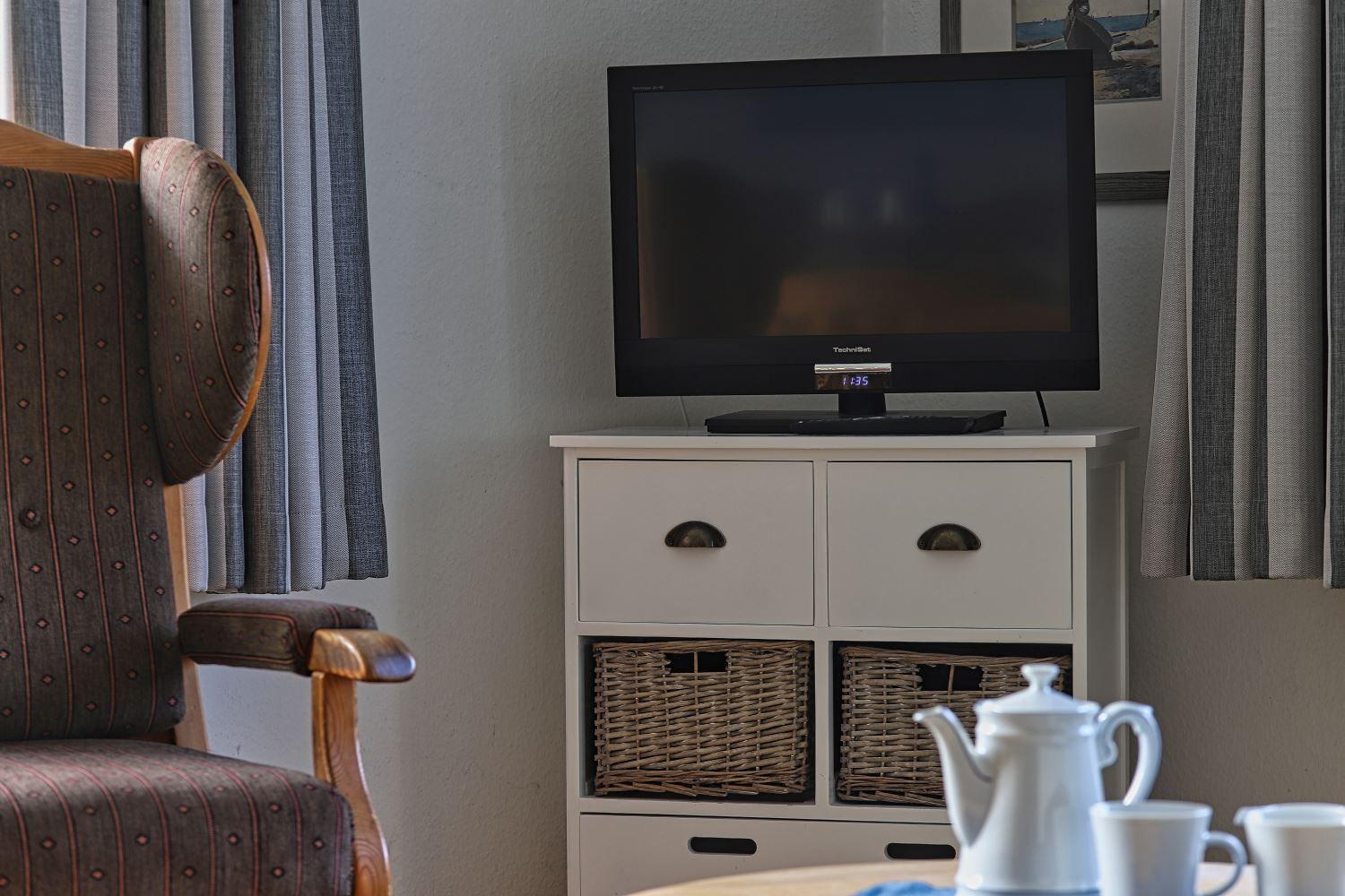 Ein Fernseher auf einem weißen Schrank mit Körben und einem Stuhl im Hintergrund.