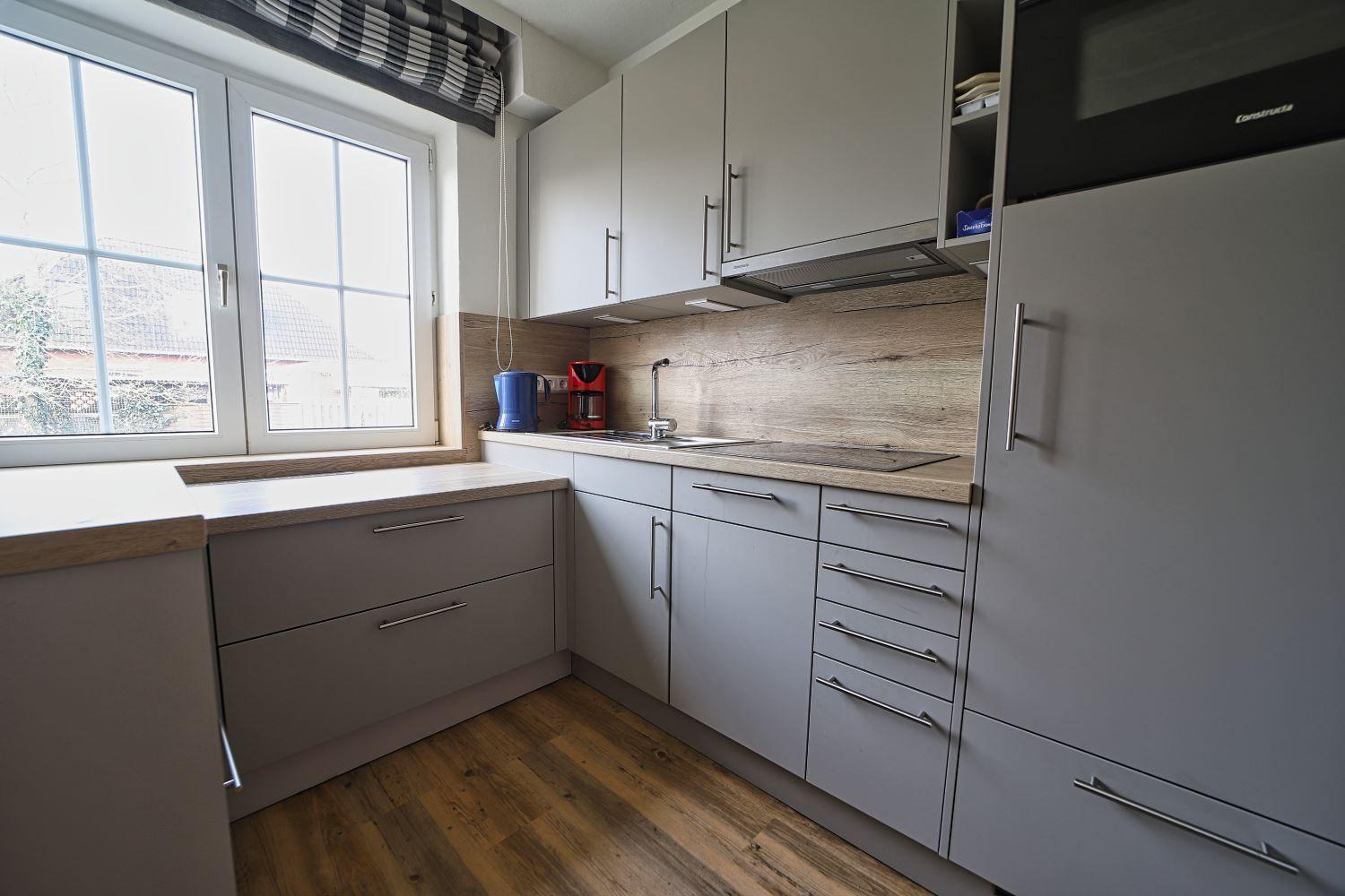 Küche mit hellen Schränken, Holzboden und Fenster mit Blick nach draußen.