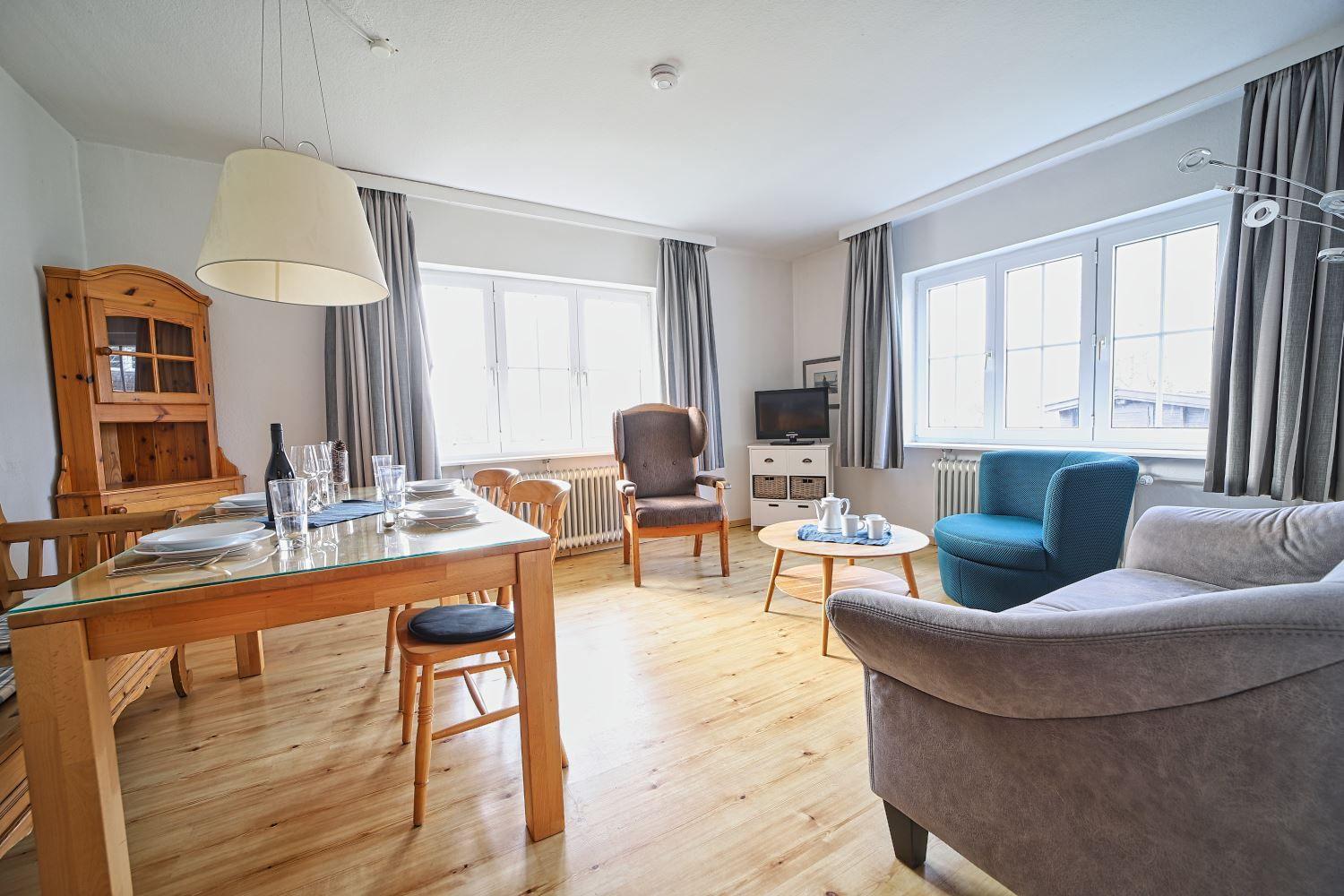 Wohn- und Essbereich mit Holzboden, Sitzgelegenheiten und Fenstern.