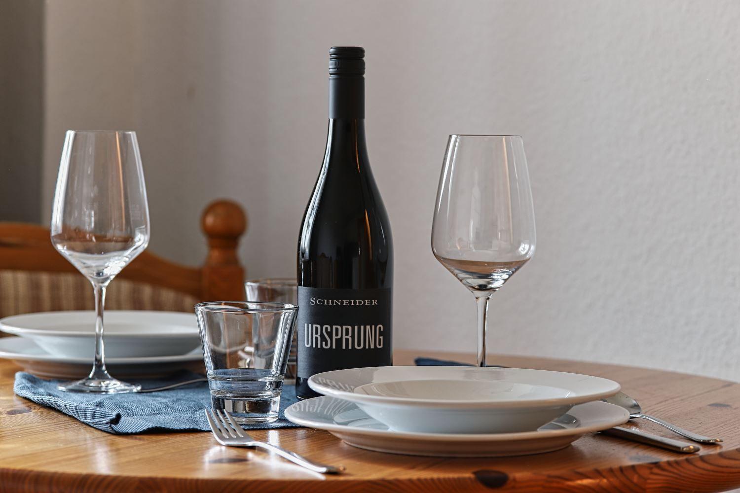 Tisch gedeckt mit Weinglas, Flasche und Geschirr.