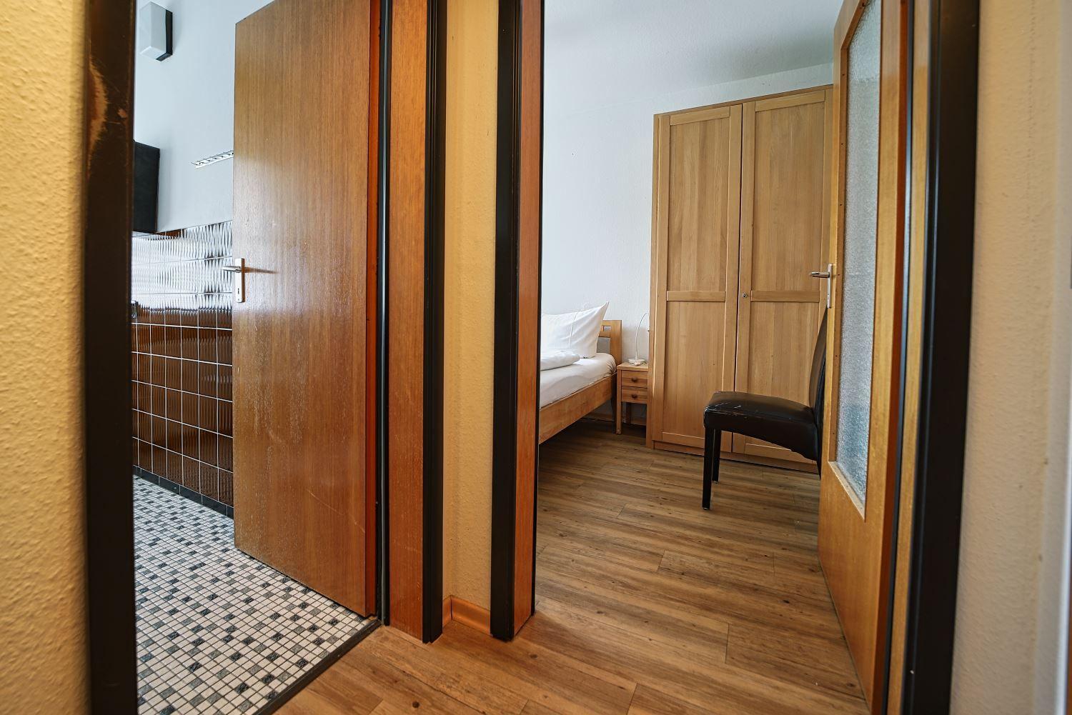 Schlafzimmer mit Bett, Kleiderschrank und Stuhl. Flur mit Holzboden und Mosaikfliesen.