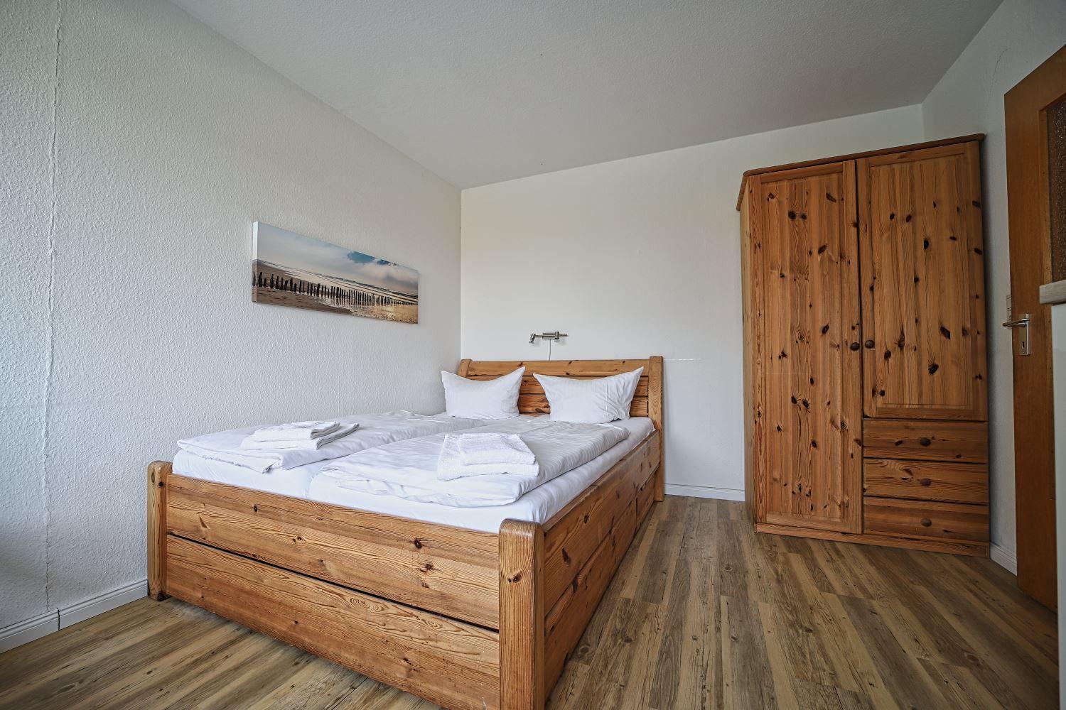 Ein Schlafzimmer mit Holzbett, Kleiderschrank und Wandbild.