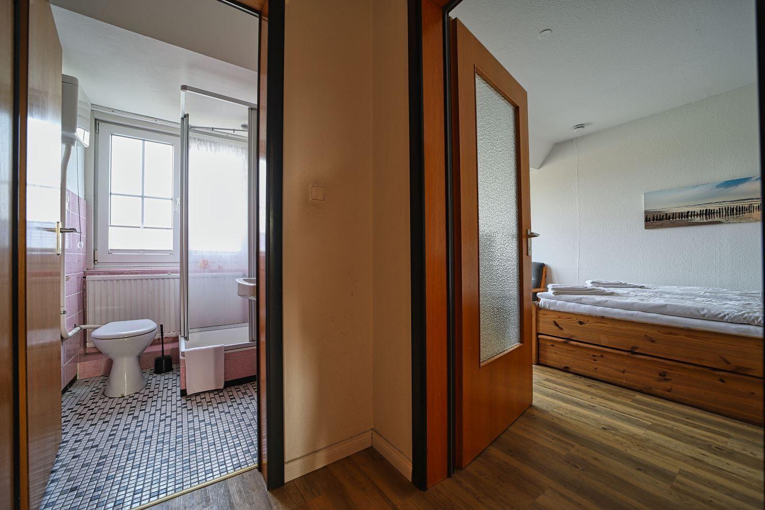 Schlafzimmer mit Holzbett und angrenzender Badewanne mit Toilette.