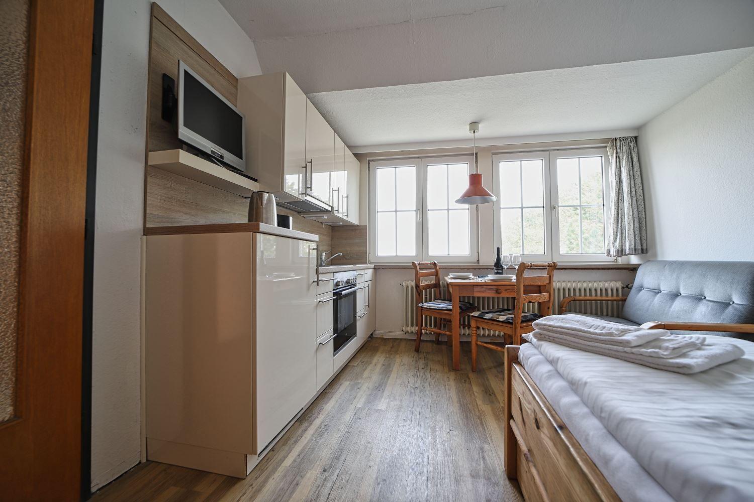 Küche mit Essbereich und Schlafsofa. Holzboden und große Fenster.