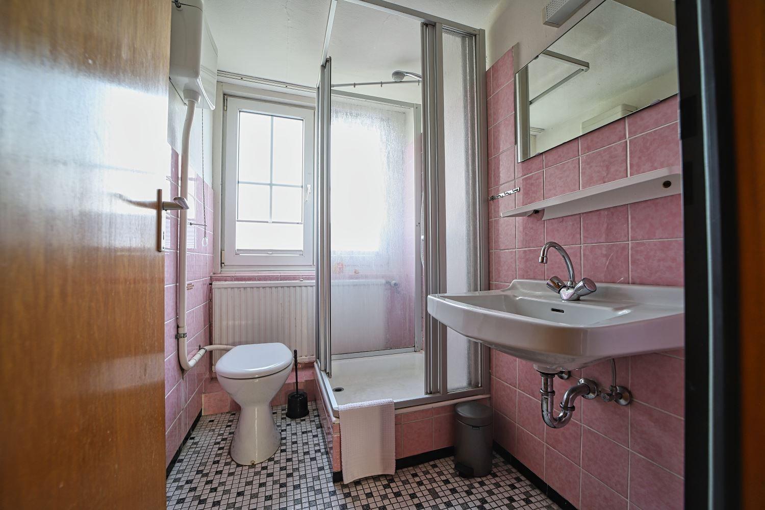 Badezimmer mit Dusche, Waschbecken und Toilette. Wände rosa gefliest.