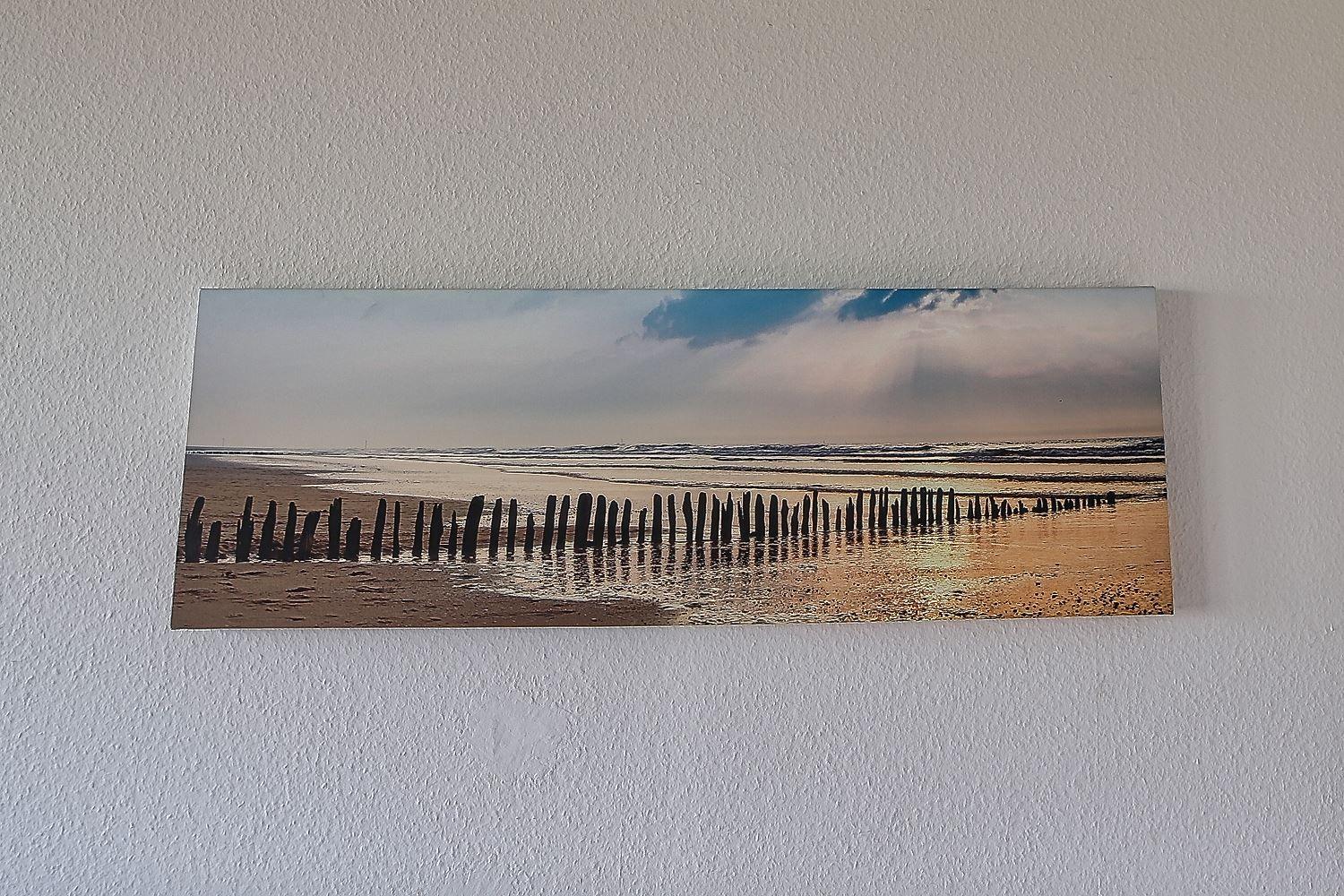 Längliches Wandbild mit Strand, Wellen und Holzpfählen im Wasser.