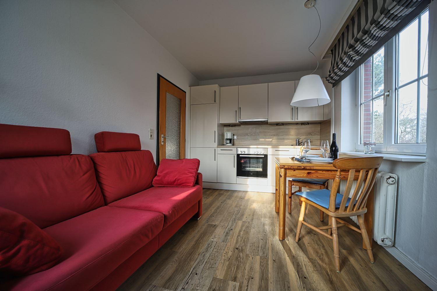 Wohnküche mit rotem Sofa, Holztisch und Küchenschränken.