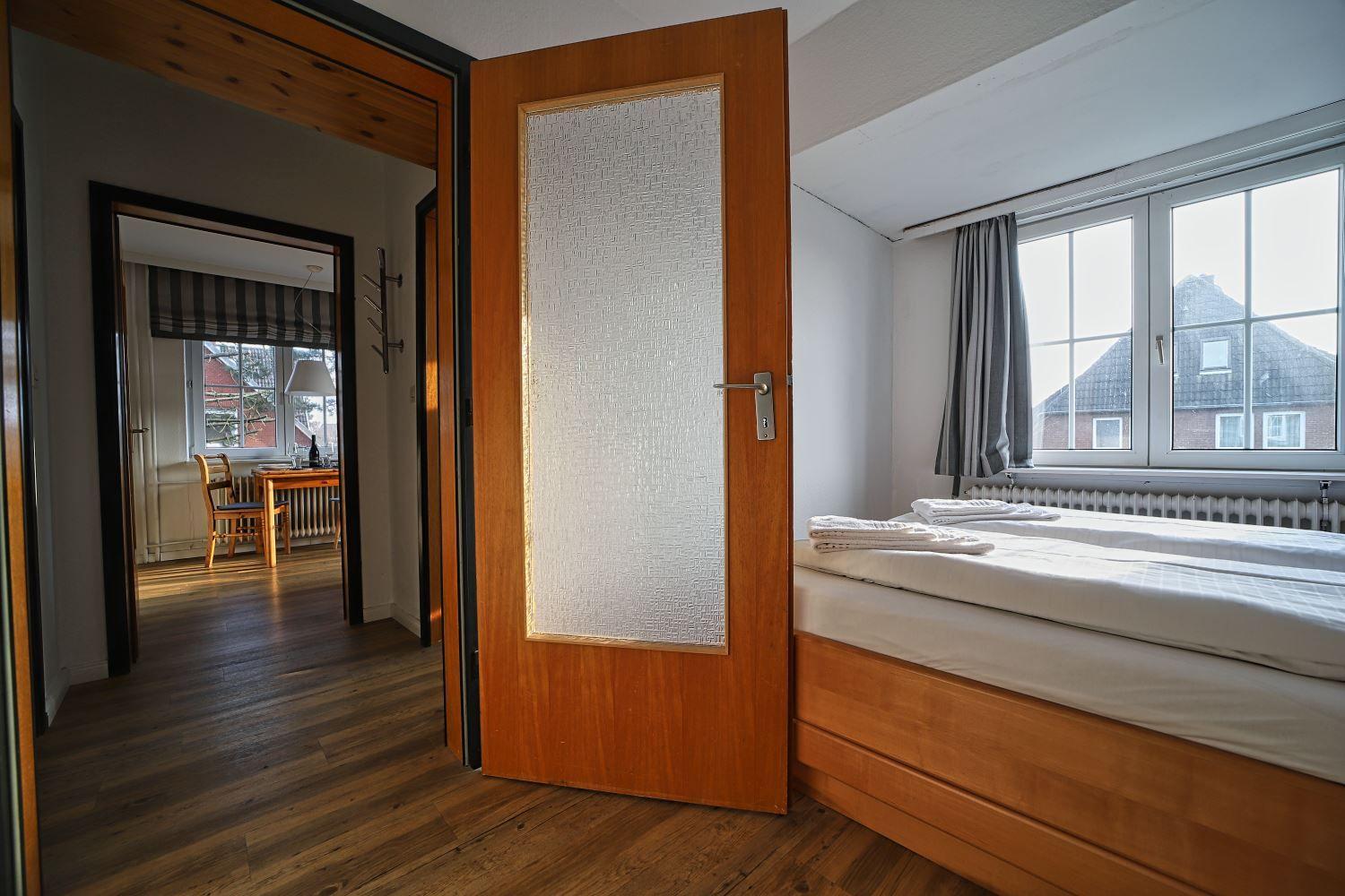 Schlafzimmer mit Bett, Fenster und Tür zur Küche.