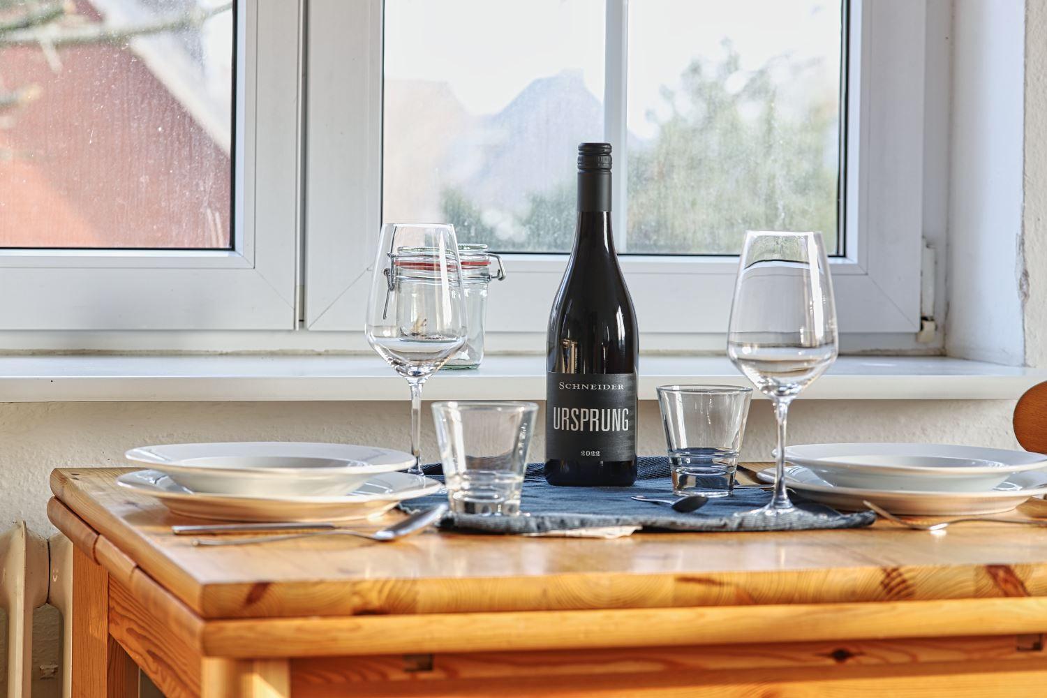 Tisch mit Weinflasche und Gläsern vor Fenster mit Bergblick