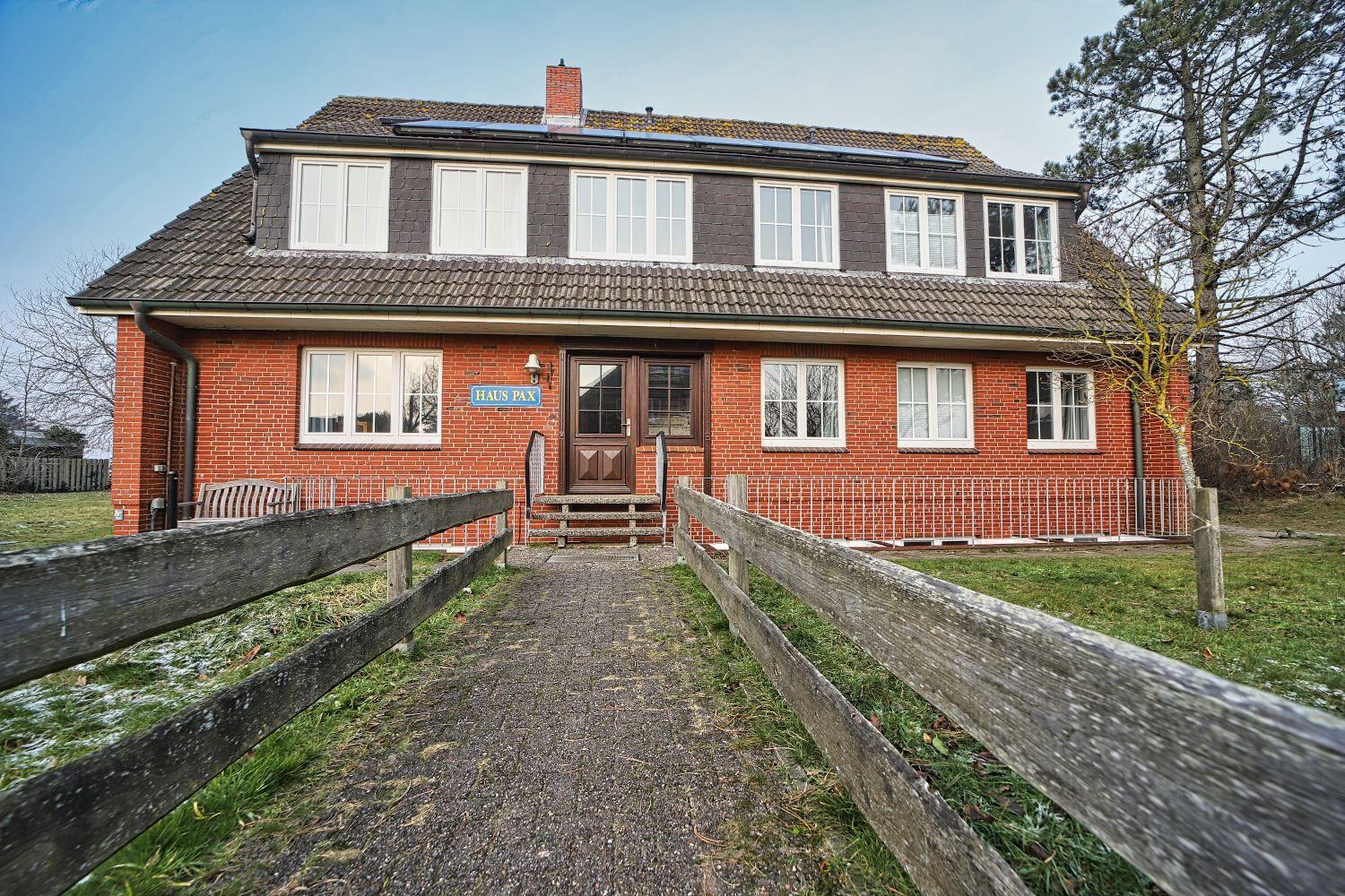 Rotes Backsteingebäude mit Holztor und Gartenweg. Hausname HAUS PAX.