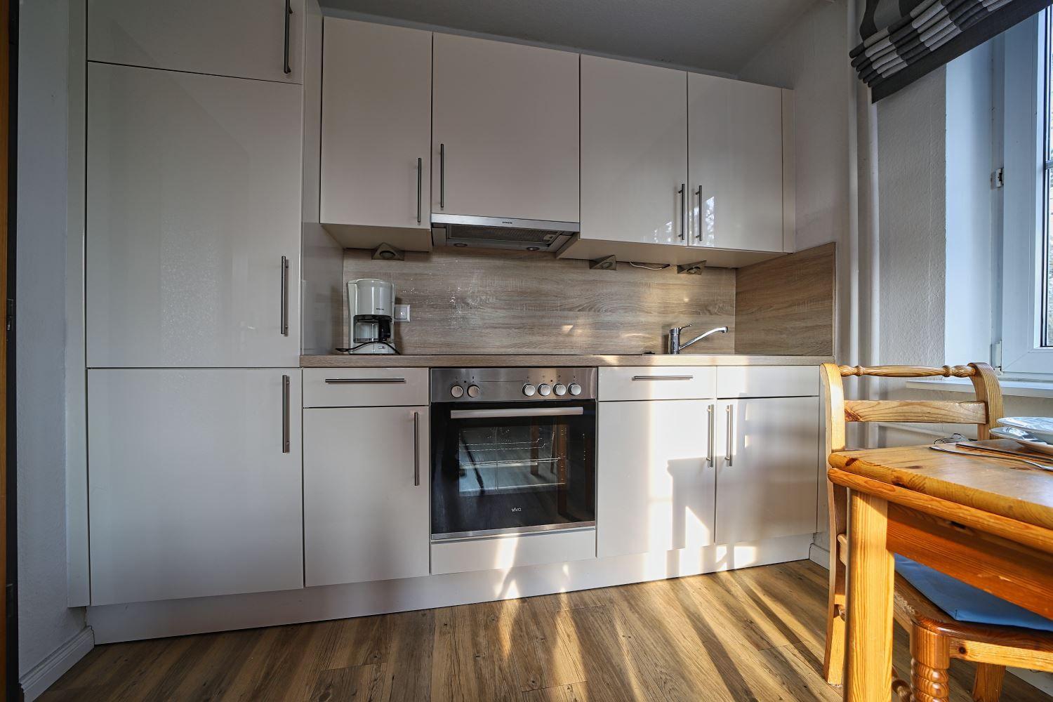 Küche mit weißen Schränken, Herd und Holztisch.