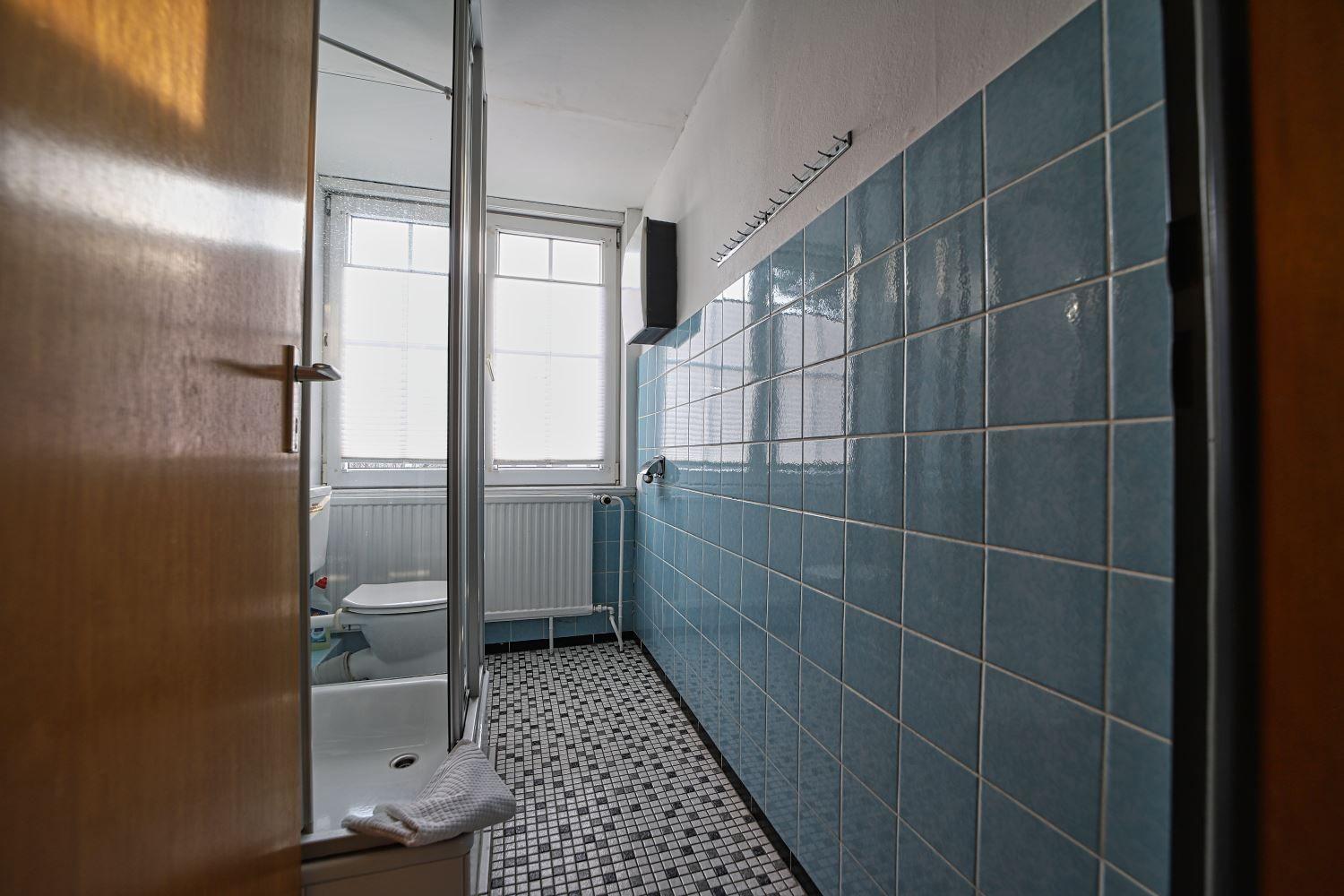 Badezimmer mit blauen Fliesen, Mosaikboden und Fenster mit Jalousie.