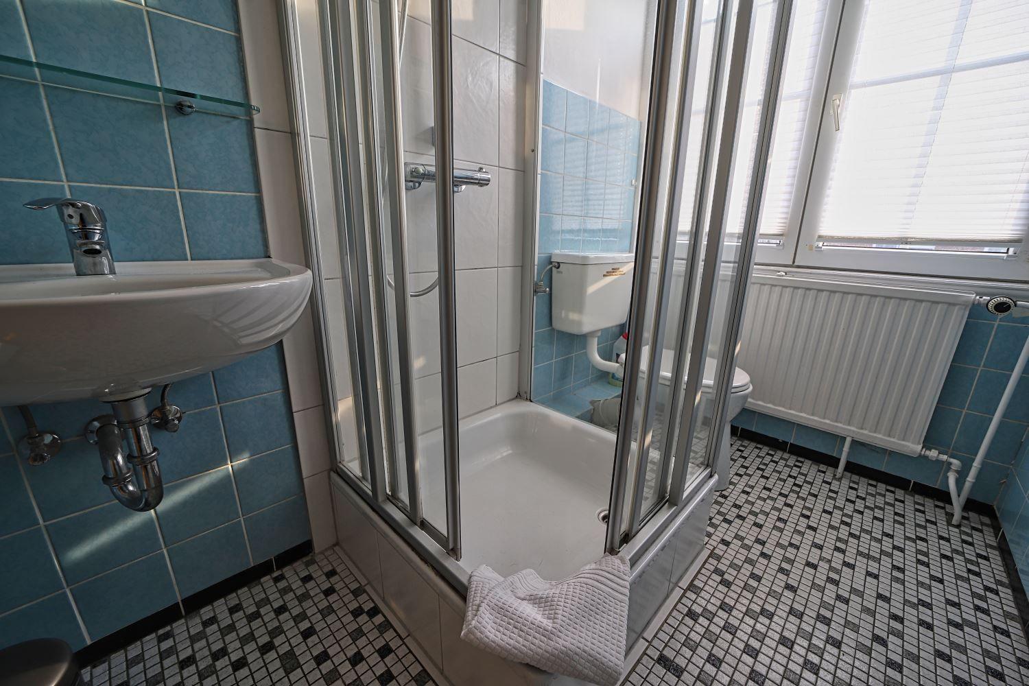 Badezimmer mit Dusche, Waschbecken und Toilette. Fliesenboden und blaue Wände.