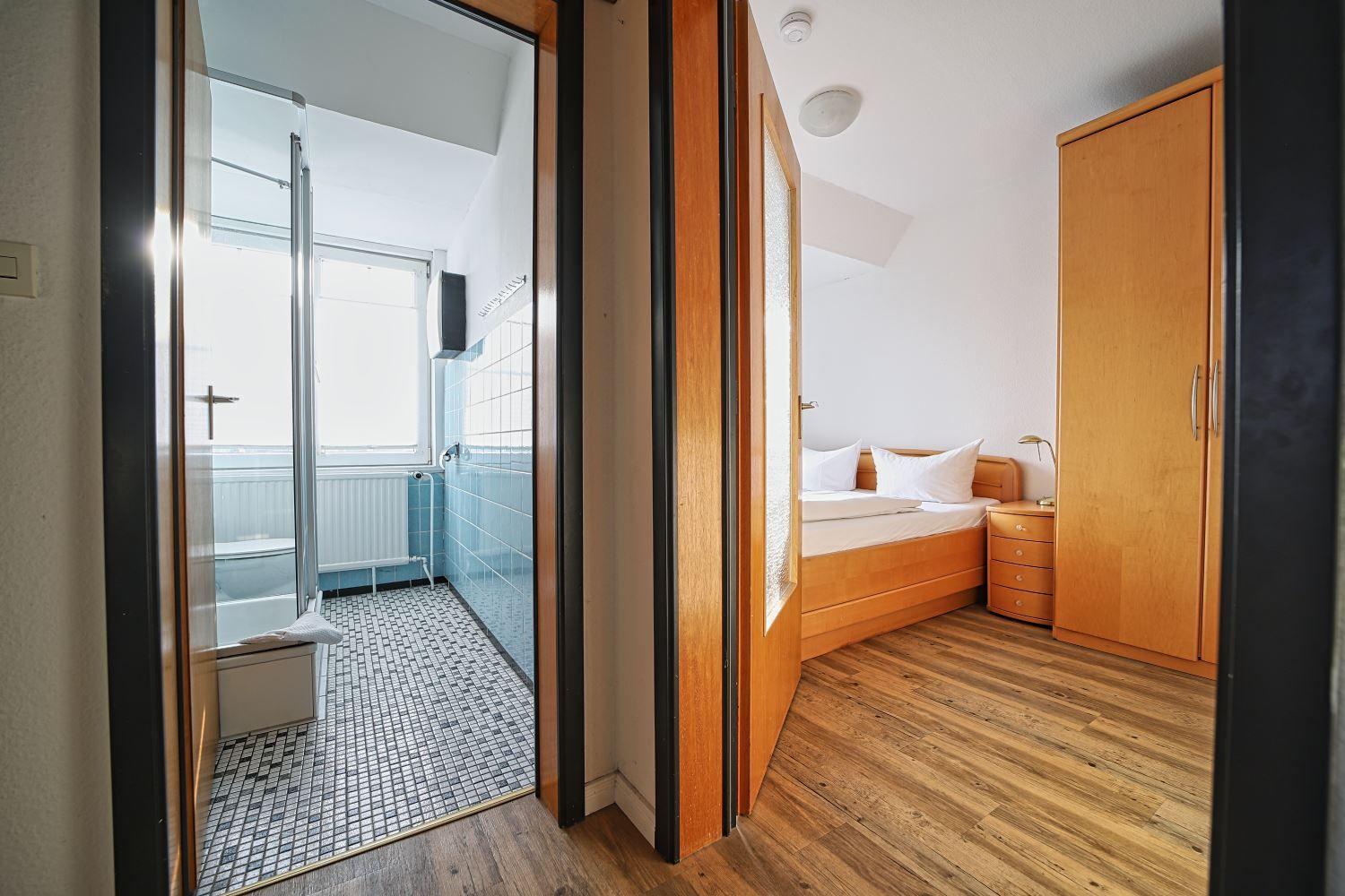 Schlafzimmer mit Holzboden und Schlafplatz. Nebenraum ist die Badewanne mit Dusche.