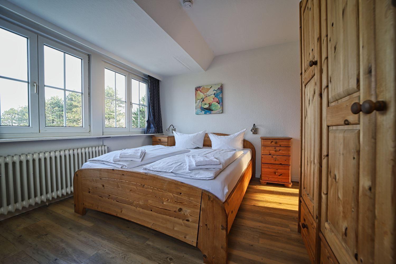 Schlafzimmer mit Holzbett, Fenster und Kleiderschrank.
