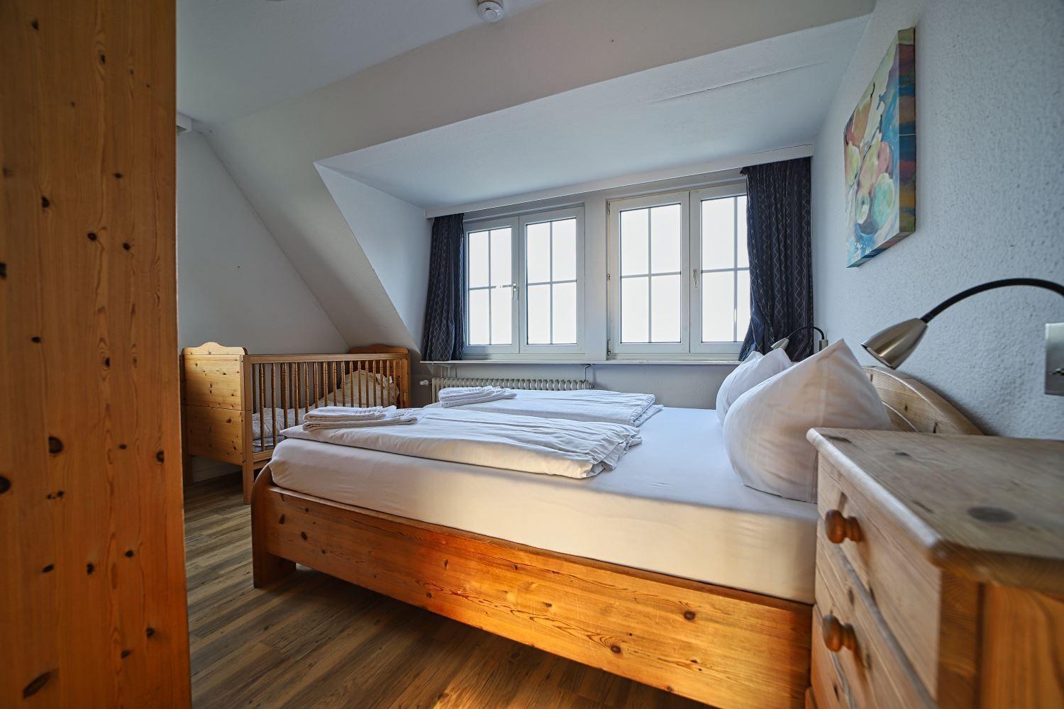 Schlafzimmer mit Holzbett, Kinderbett und Fenster.